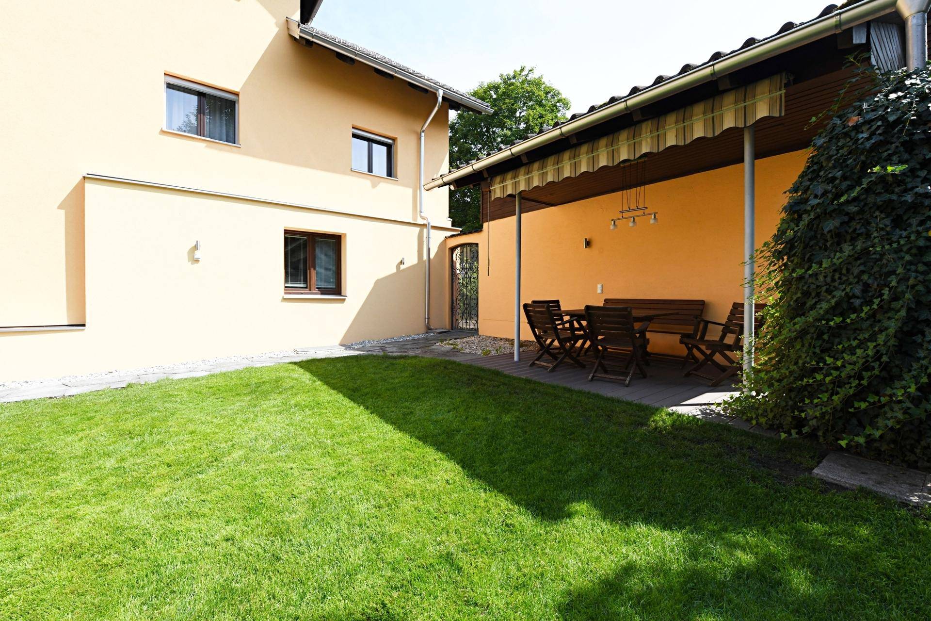 Gepflegter Gartenbereich mit Rasenfläche und überdachter Terrasse mit Sitzgelegenheiten am Haus.