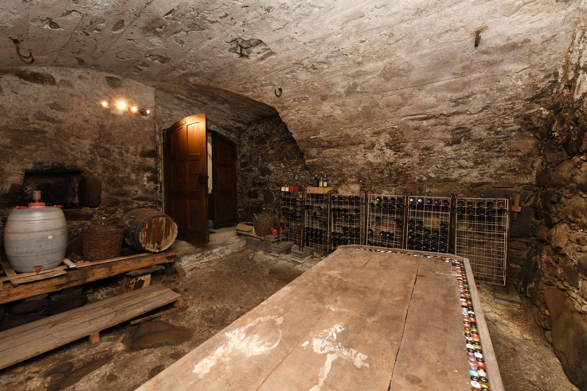 Historischer Weinkeller mit Steinwänden, Holztisch und Weinregalen für Lagerung.