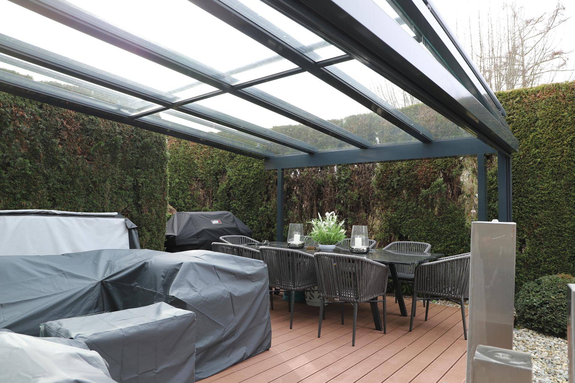 Überdachter Essbereich im Freien mit großem Tisch und Stühlen, umgeben von einer Hecke.