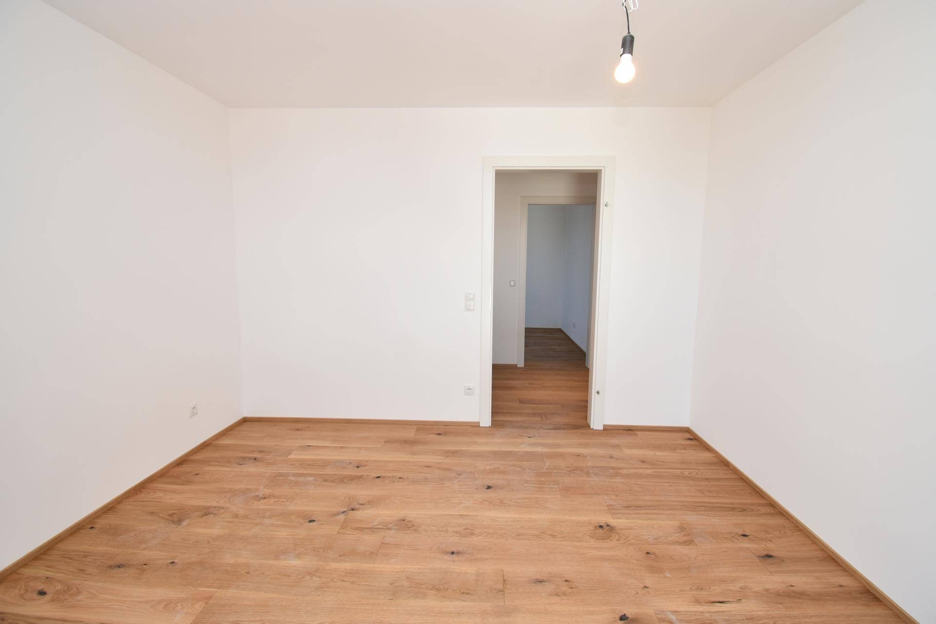 Leeres Schlafzimmer mit hellem Holzparkettboden und weiß gestrichenen Wänden.