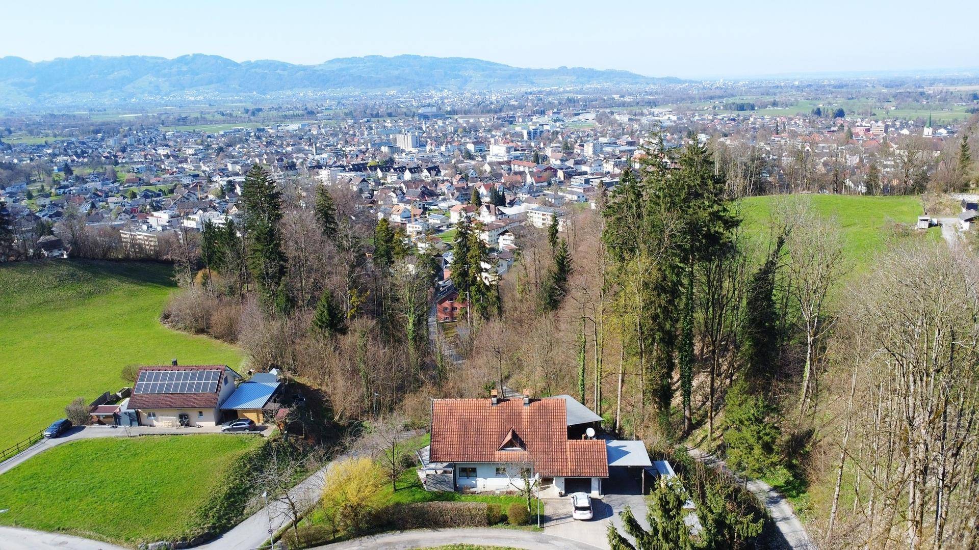 Luftaufnahme eines Einfamilienhauses mit rotem Ziegeldach, umgeben von Natur und mit Fernblick.