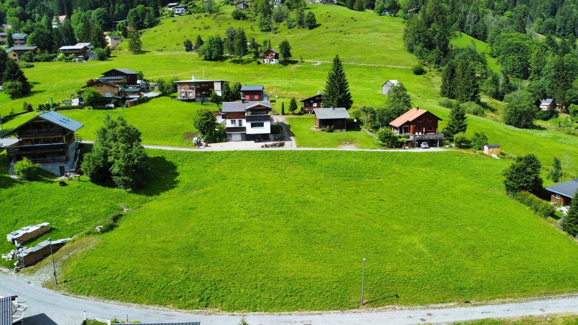 Luftaufnahme eines großen grünen Grundstücks mit umliegenden Häusern in einer bergigen Landschaft.