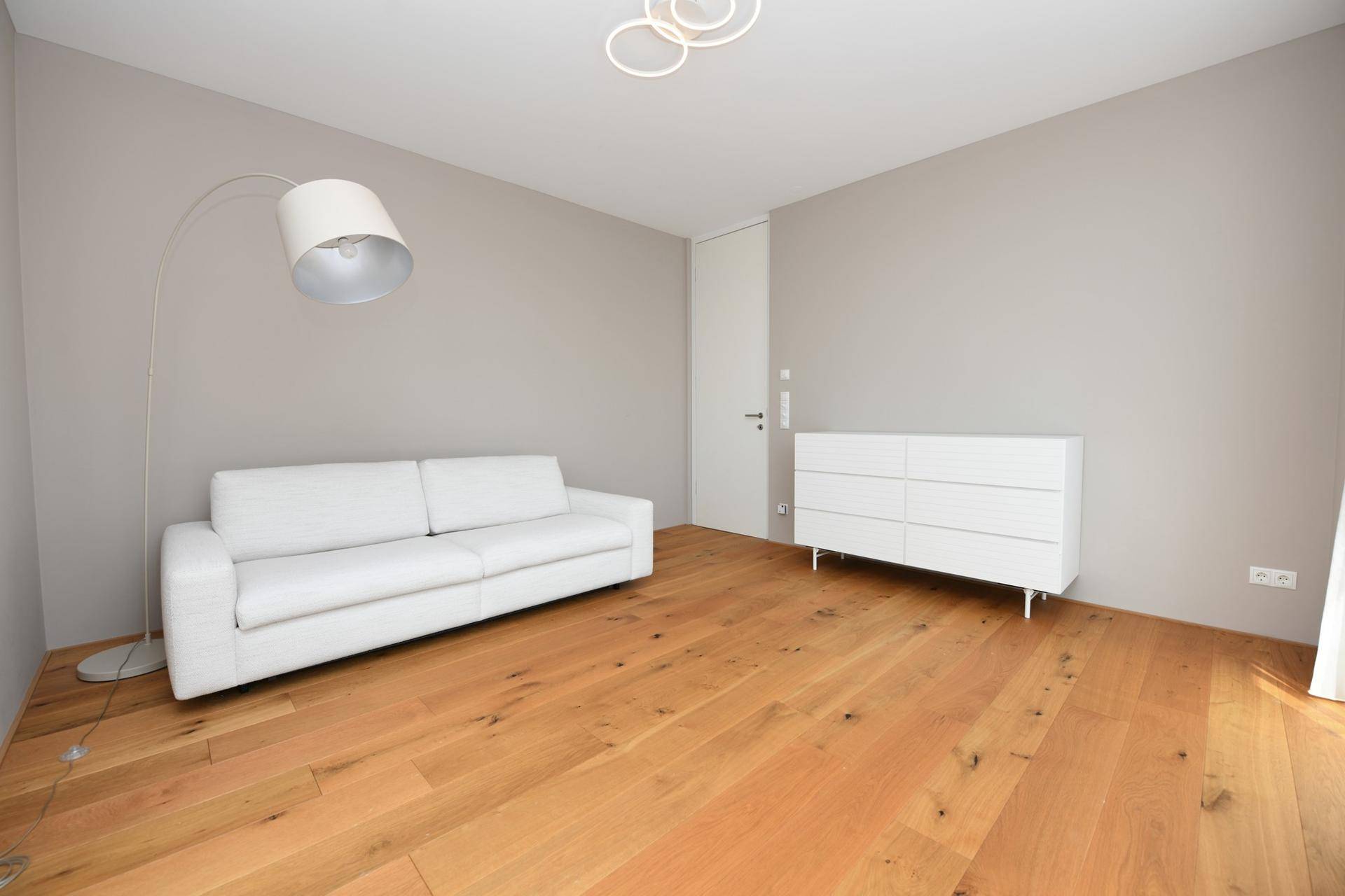 Freundliches Zimmer mit modernem Sofa, Stehlampe und hellem Holzboden.