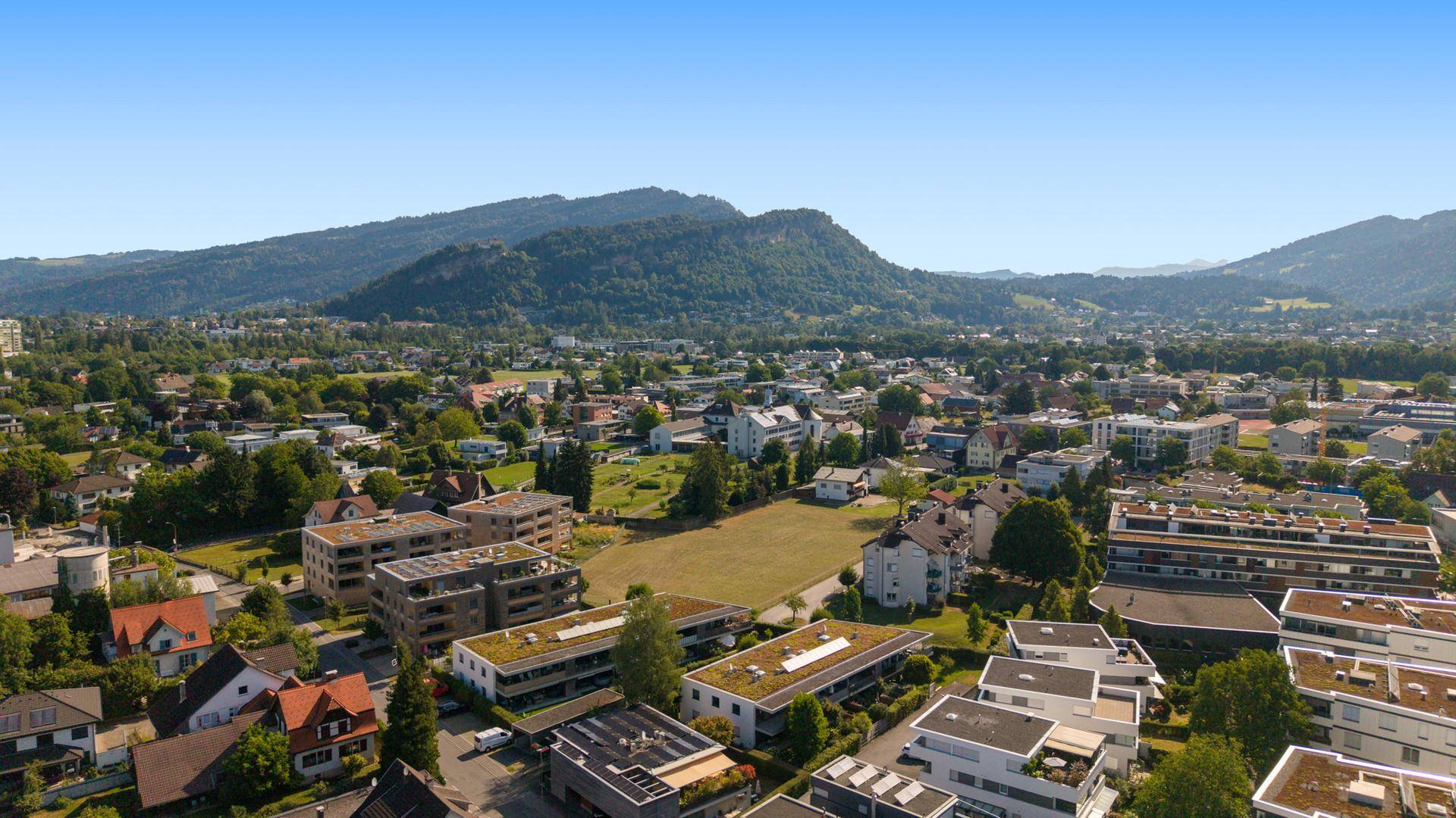 Weitläufige Luftaufnahme einer Stadt mit Wohngebäuden und Bergen im Hintergrund.