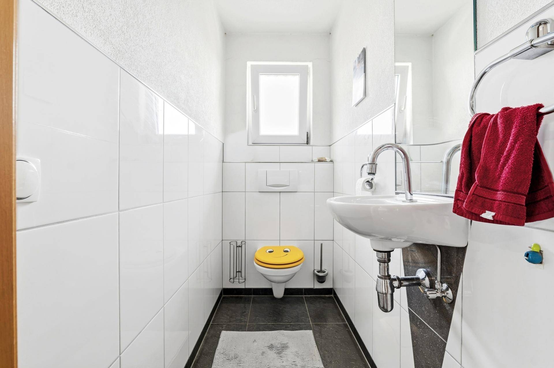 Kleines Gäste-WC mit Fenster, Waschbecken und dunklem Fliesenboden.