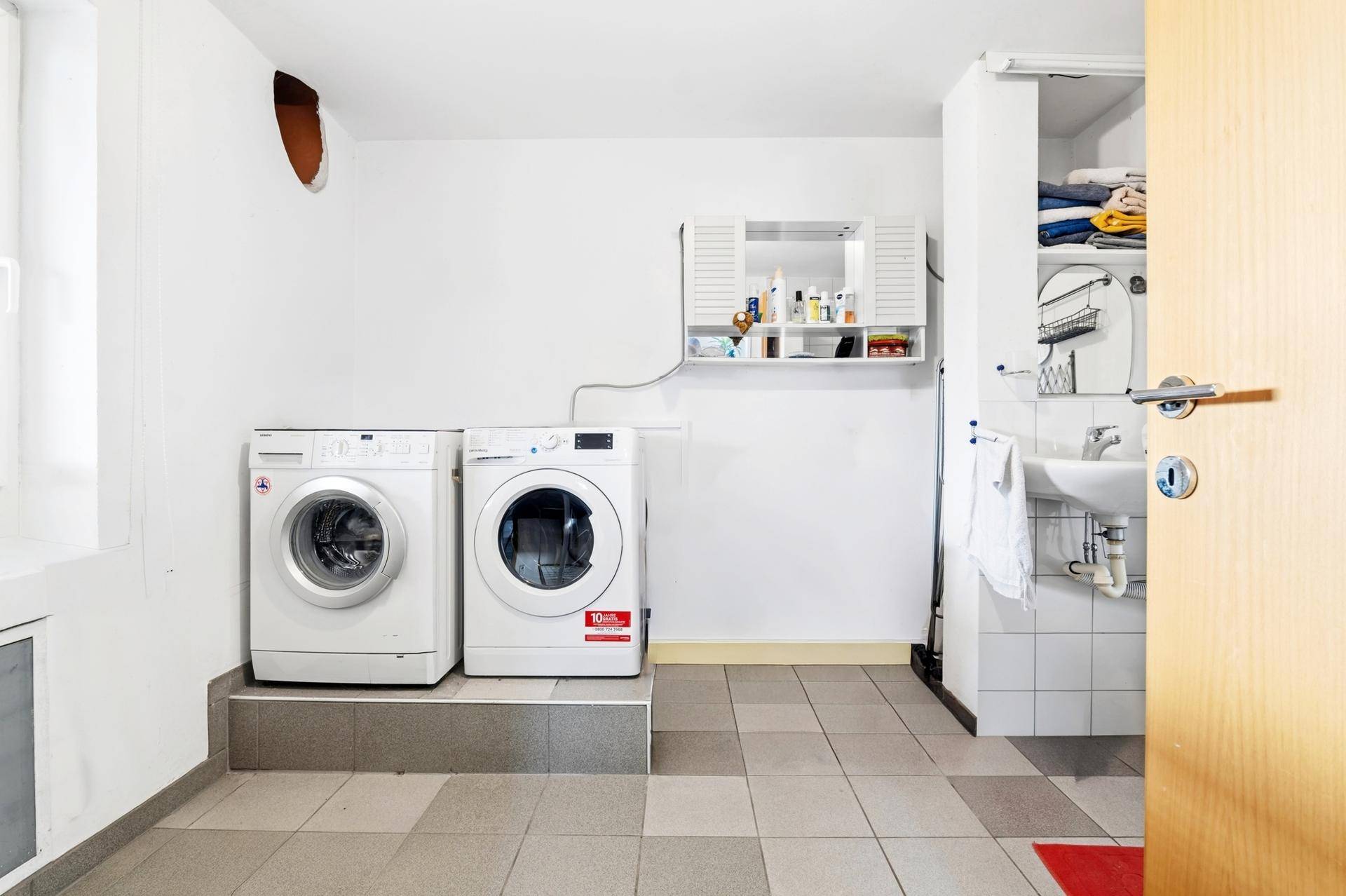 Waschküche mit Waschmaschinen, Trockner und Waschbecken.