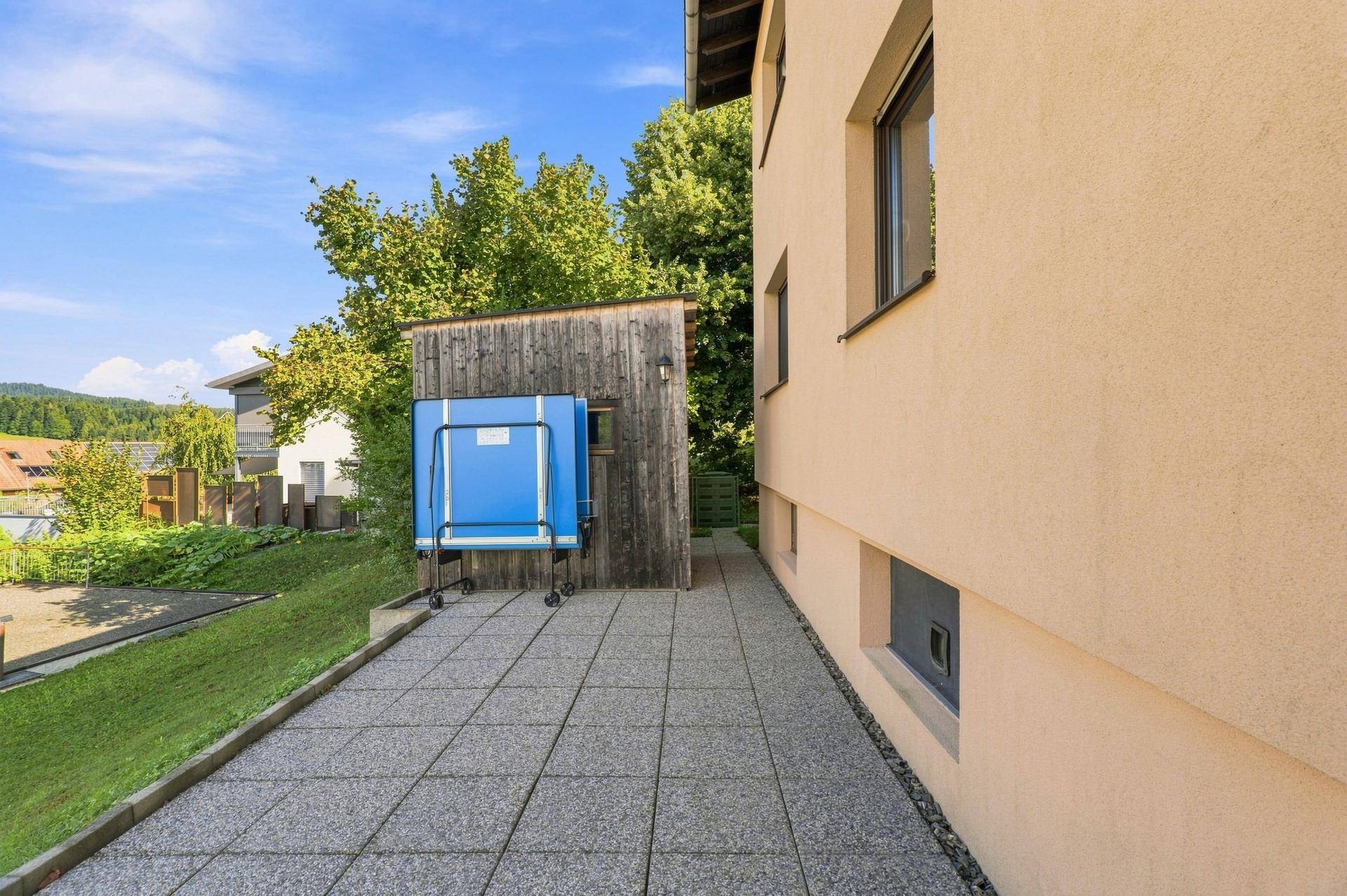 Seitliche Terrasse mit gepflastertem Bereich, angrenzendem Rasen und einem Gartenschuppen.