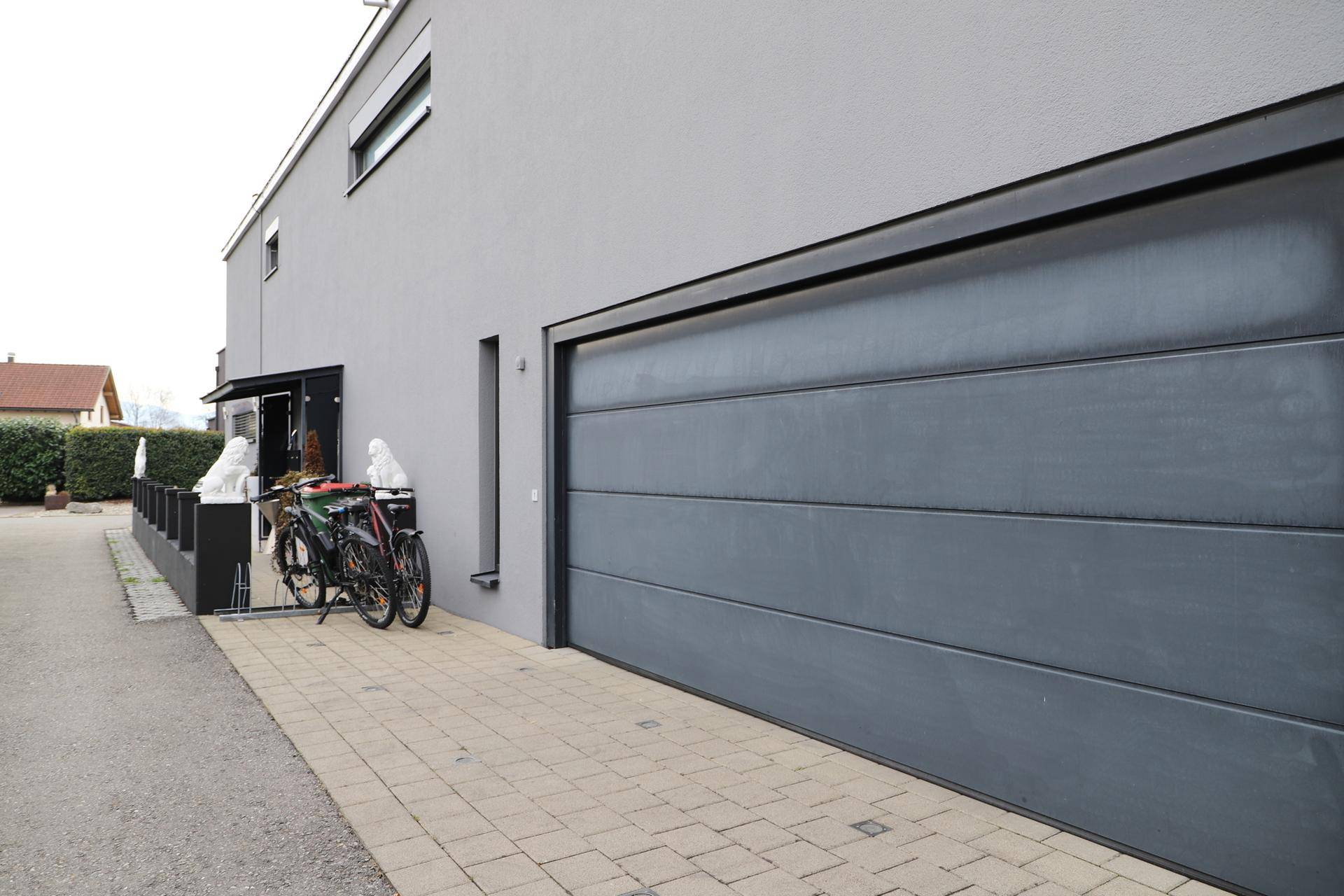 Moderne Gebäudefassade mit großer grauer Garage und gepflasterter Zufahrt.
