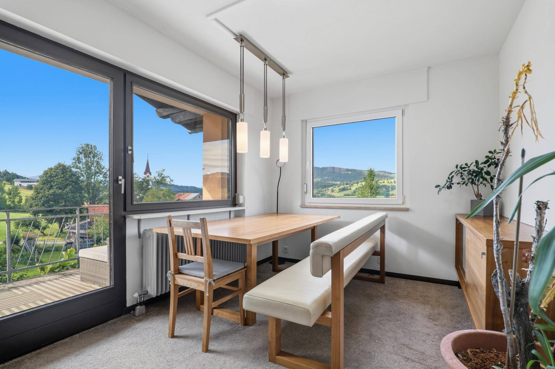 Heller Essbereich mit Holztisch, Sitzbank und großem Fenster mit Bergblick.