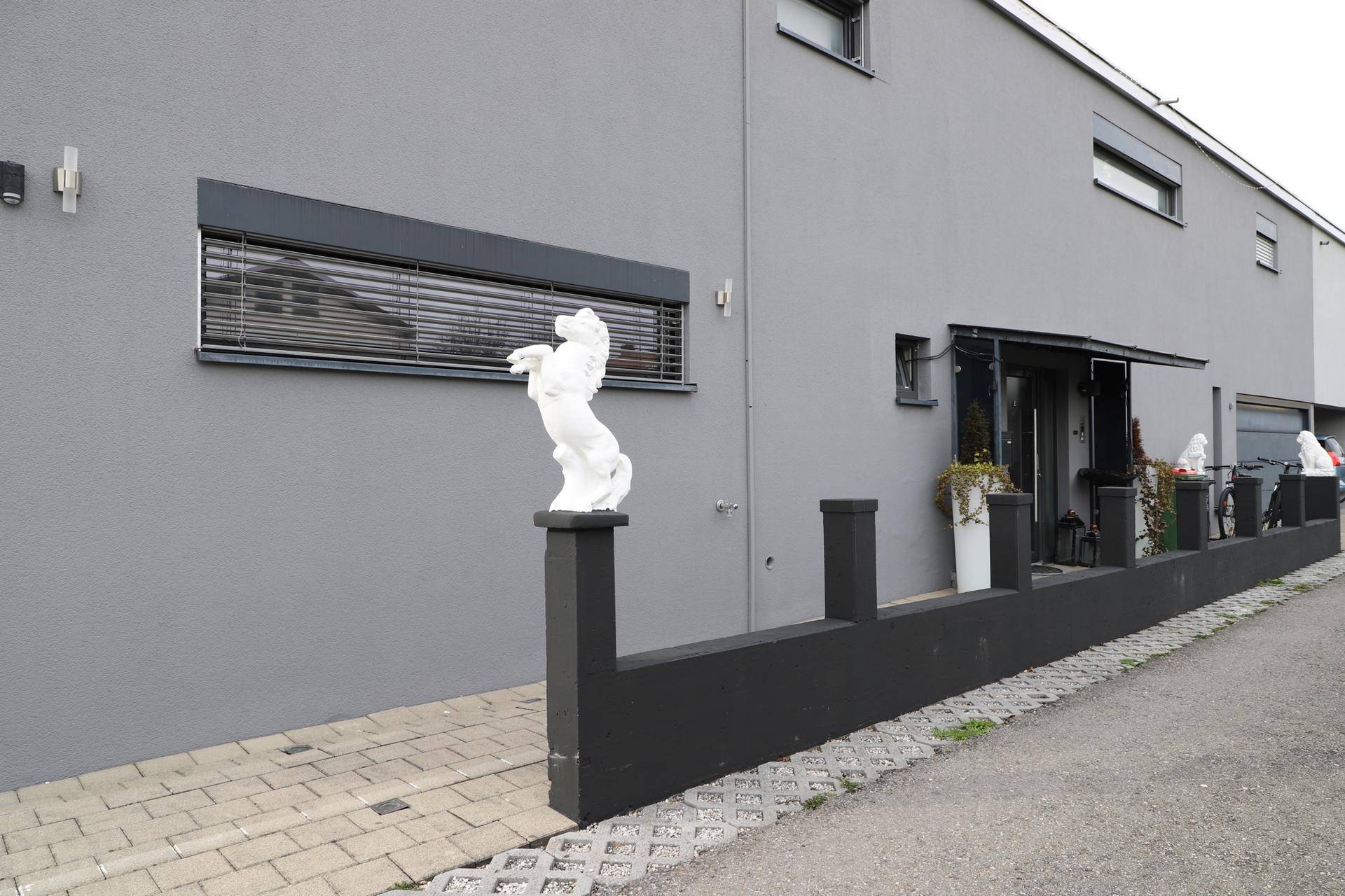 Graue Gebäudefassade mit modernen Fenstern, Rollläden und dekorativen Statuen.