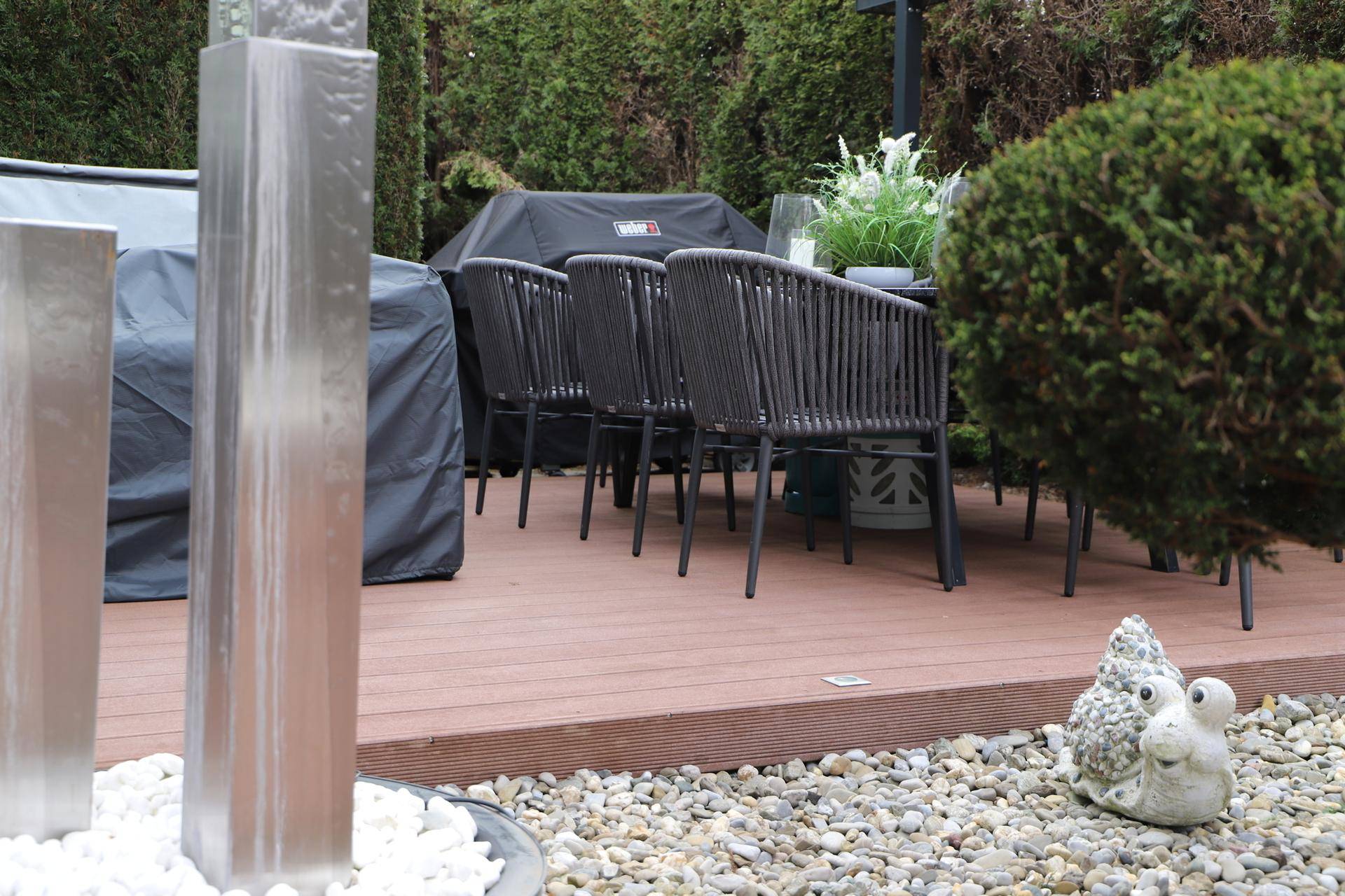 Gedeckter Esstisch im Freien mit Wasserspiel und dekorativem Gartenzwerg für gemütliche Abende.
