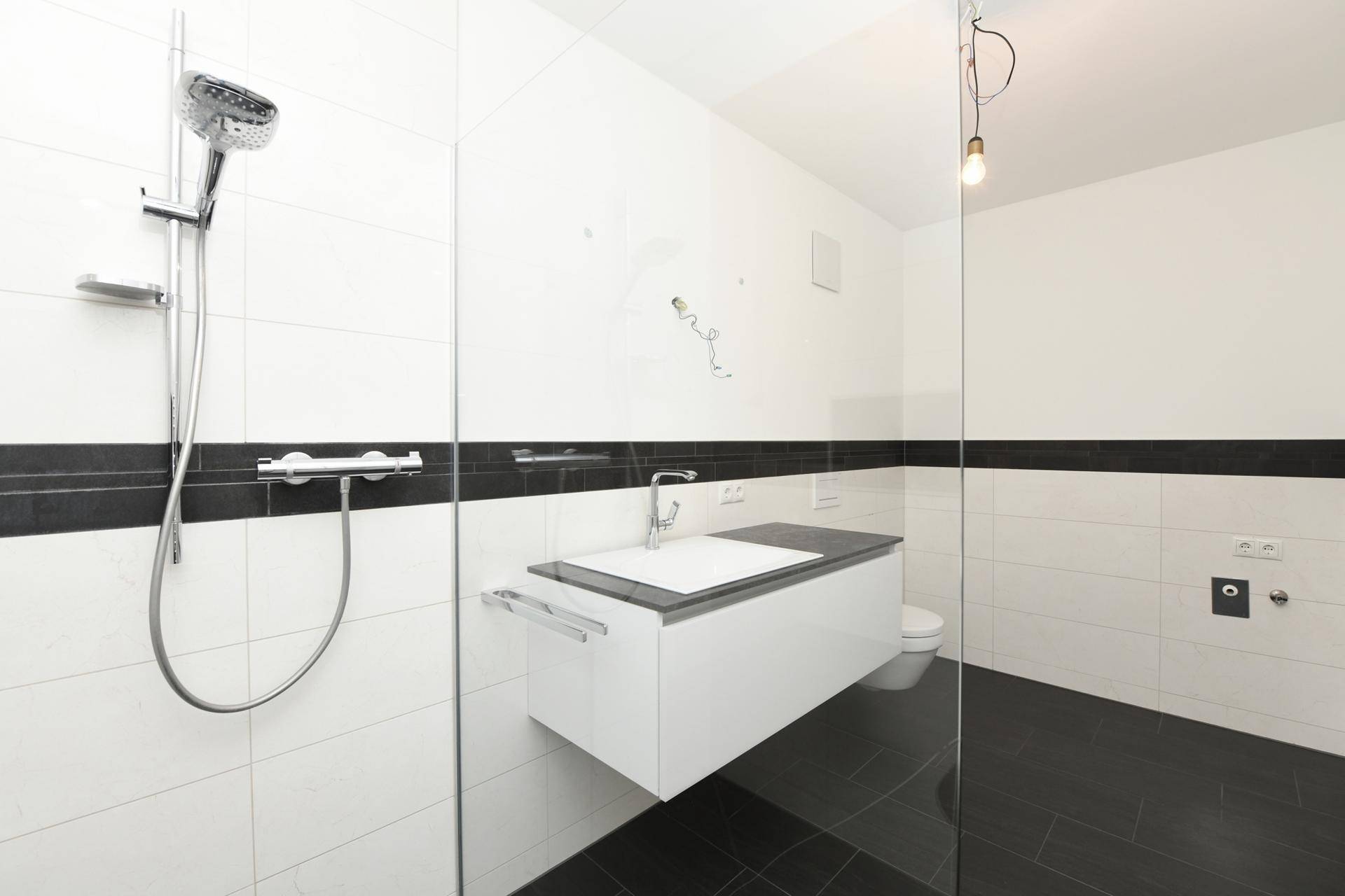 Geräumige, moderne Dusche mit Glaswand und schwarzem Fliesenboden im Badezimmer.