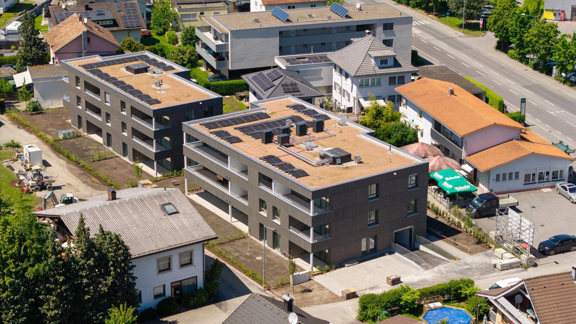 Luftaufnahme von zwei modernen Mehrfamilienhäusern mit Photovoltaikanlagen auf den Flachdächern.