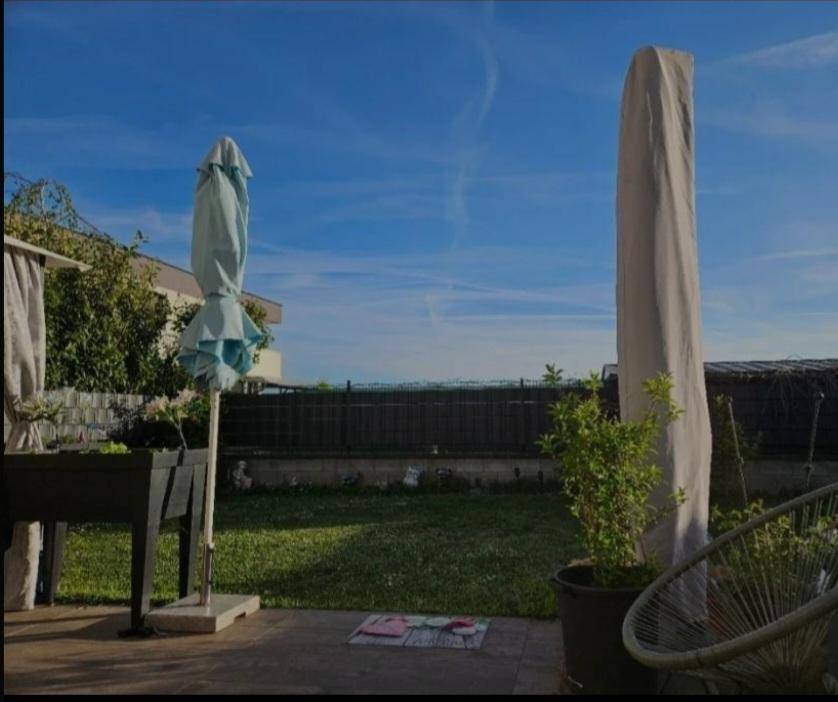 Sonniger Gartenbereich mit Rasenfläche, Terrasse und abgedeckten Gartenmöbeln.