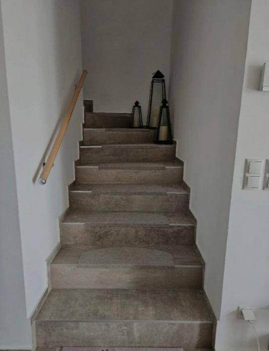 Treppenaufgang mit gefliesten Stufen und schlichtem Holzgeländer.