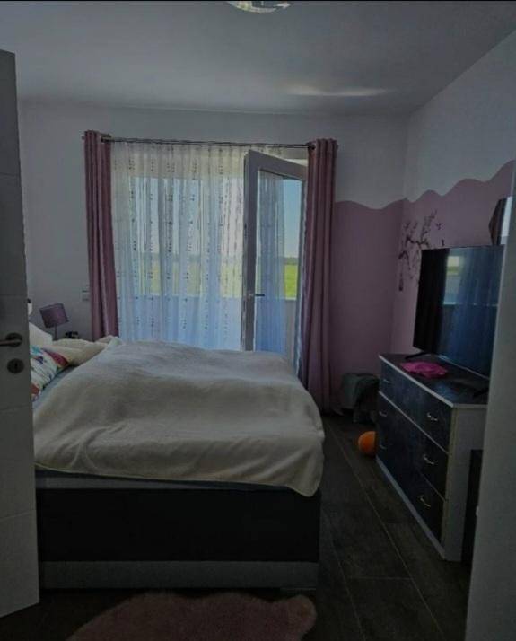 Helles Schlafzimmer mit Bett, Kommode und Zugang zu einem Balkon oder einer Terrasse.