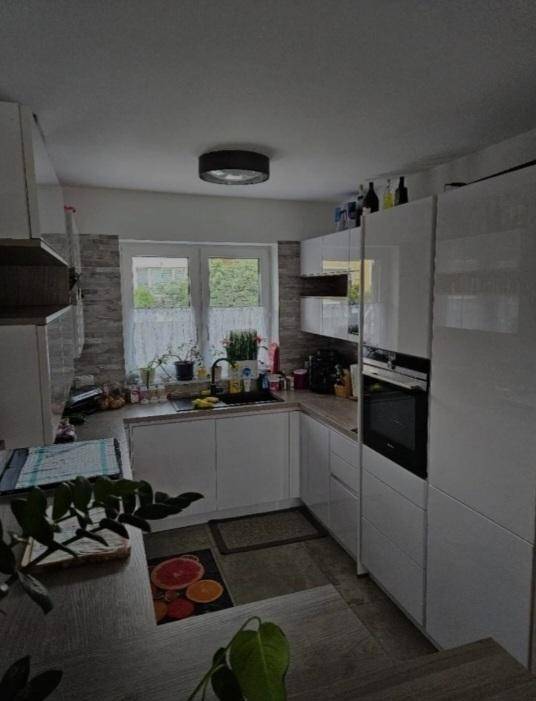 Moderne Küche mit weißen Hochglanzfronten, integriertem Backofen und Fensterblick.