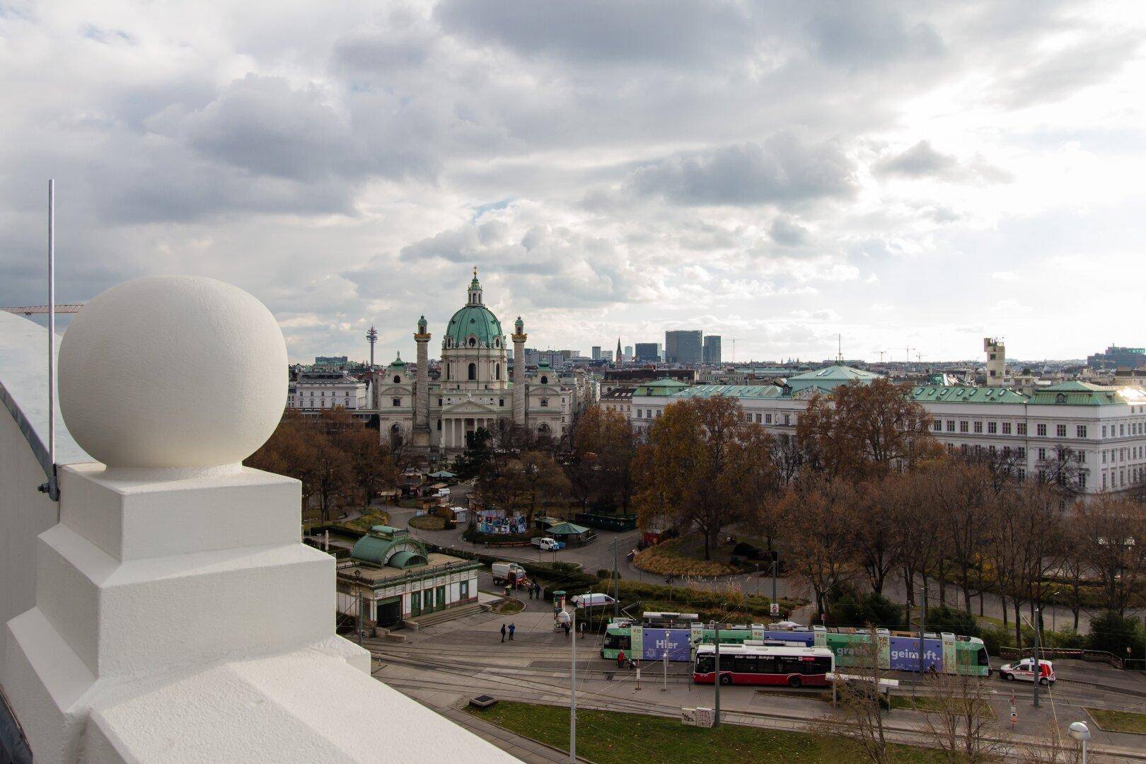 Panoramablick über die Stadt mit der Karlskirche und ihrer markanten grünen Kuppel unter bewölktem Himmel.