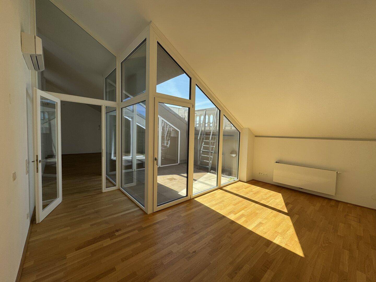 Helles Wohnzimmer mit Parkettboden, schrägen Decken und großen Glasfronten zur Terrasse.