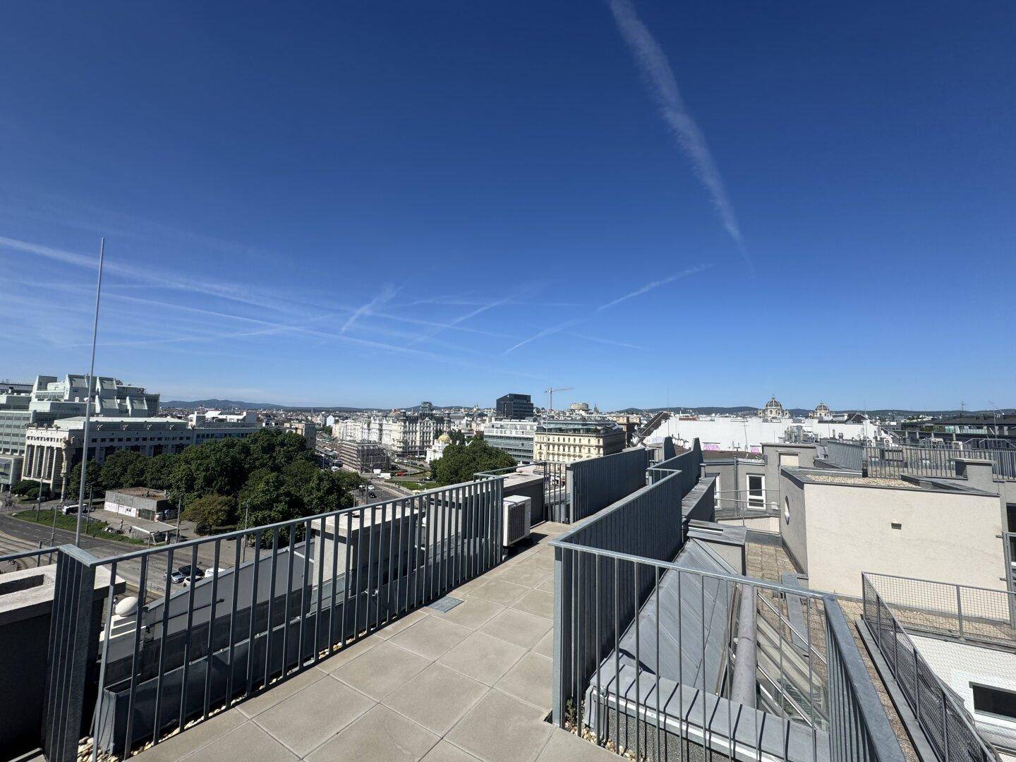 Weitläufige Dachterrasse mit Metallgeländer und Blick über die umliegenden Dächer der Stadt.