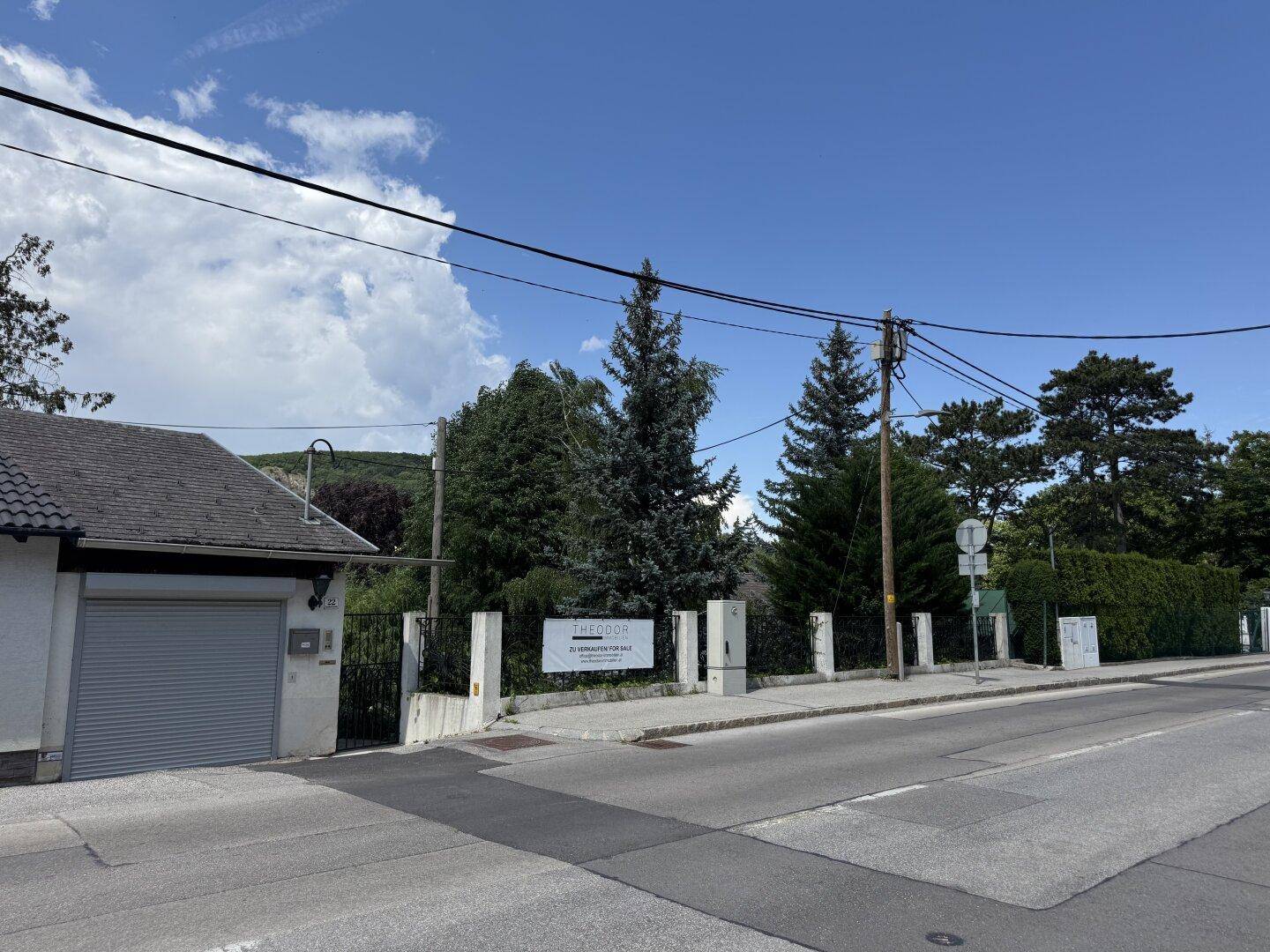 Ansicht von der Straße mit einem Haus, Garage, Zaun und einem Hinweisschild unter blauem Himmel.