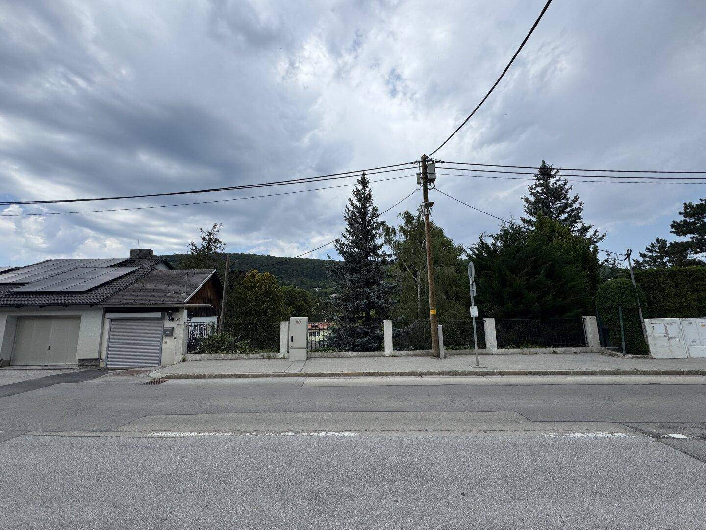 Straßenansicht des Hauses mit Garage, Zaun und der dahinterliegenden grünen Hügellandschaft.
