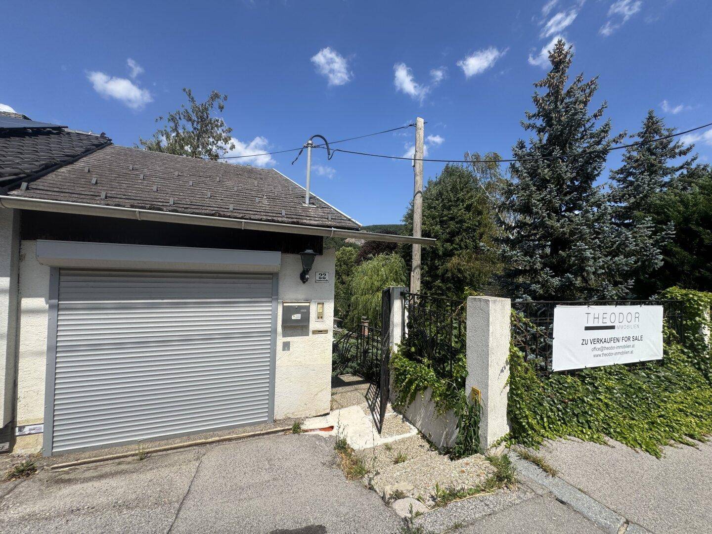 Einfahrt zum Grundstück mit Garage, Verkaufsanzeige und einer gepflegten Hecke.
