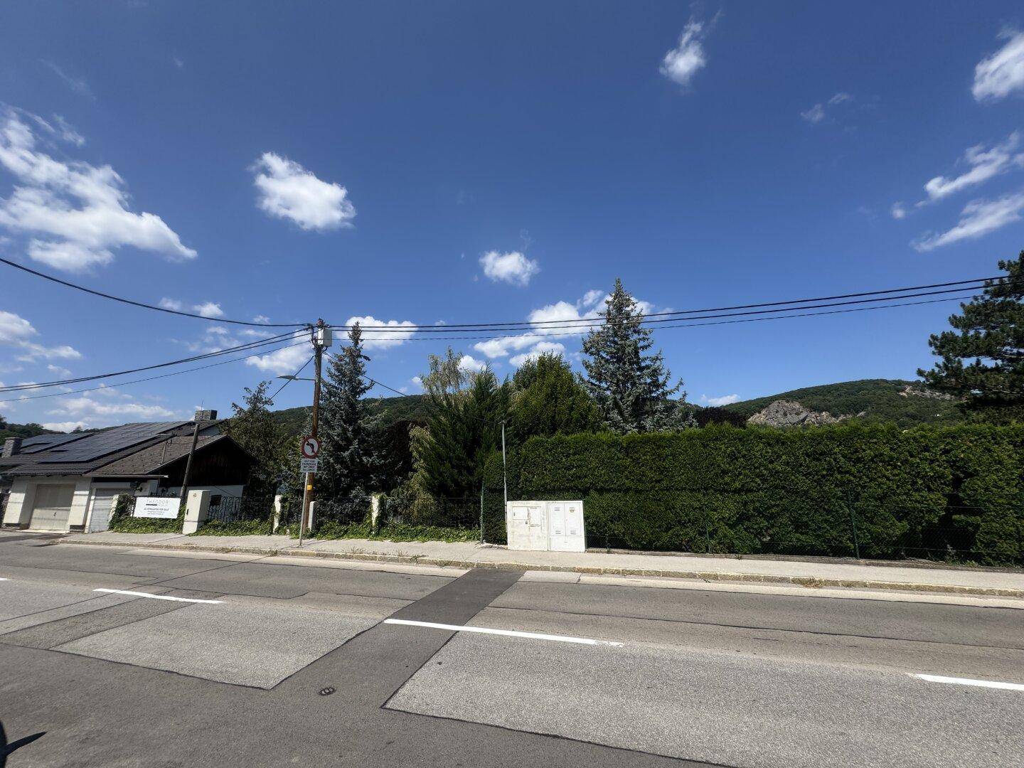 Straßenansicht des Grundstücks mit langer Hecke und Blick auf die gegenüberliegenden Hügel.