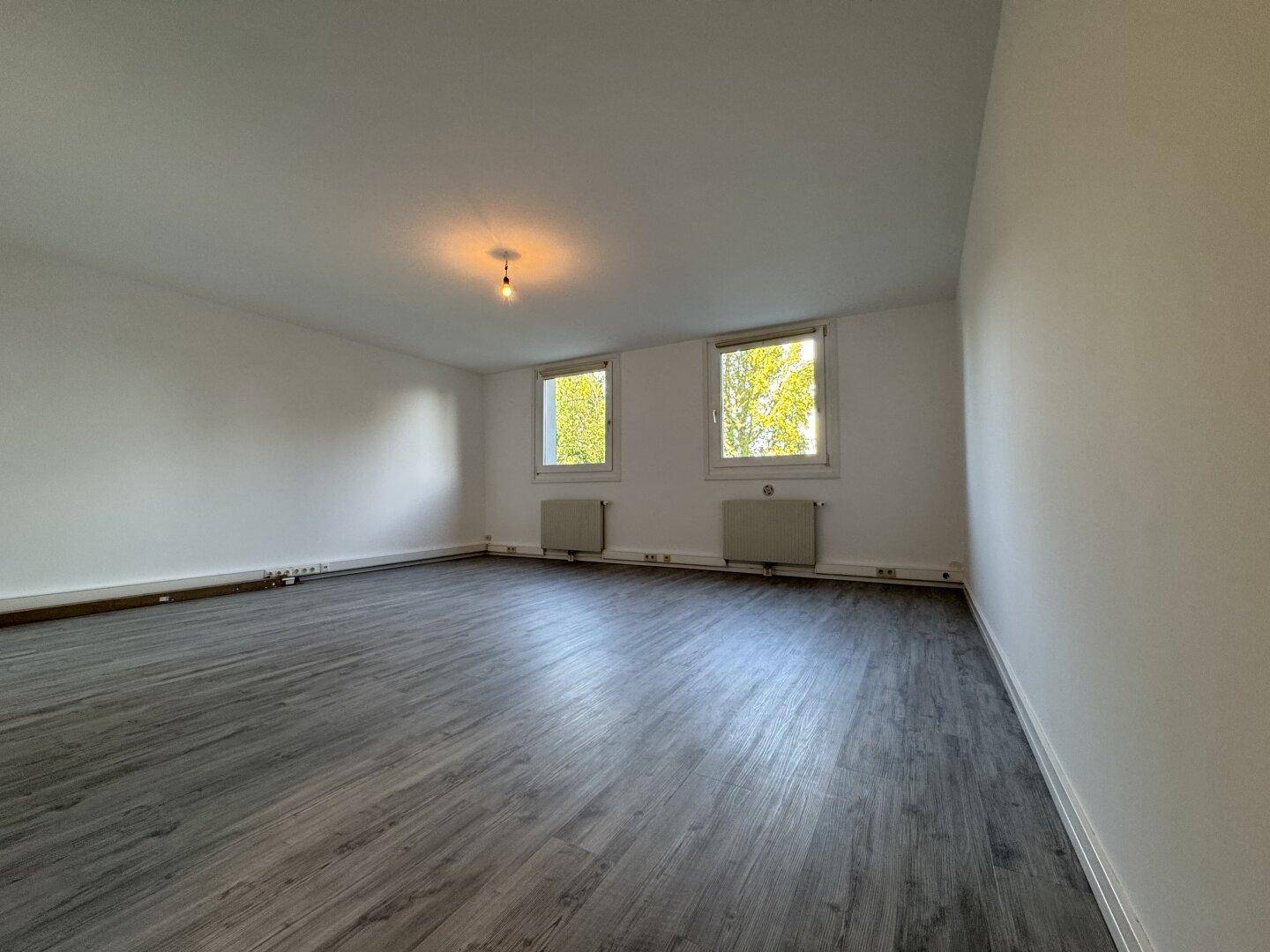 Heller, leerer Raum mit modernem Laminatboden und zwei Fenstern, die Tageslicht hereinlassen.