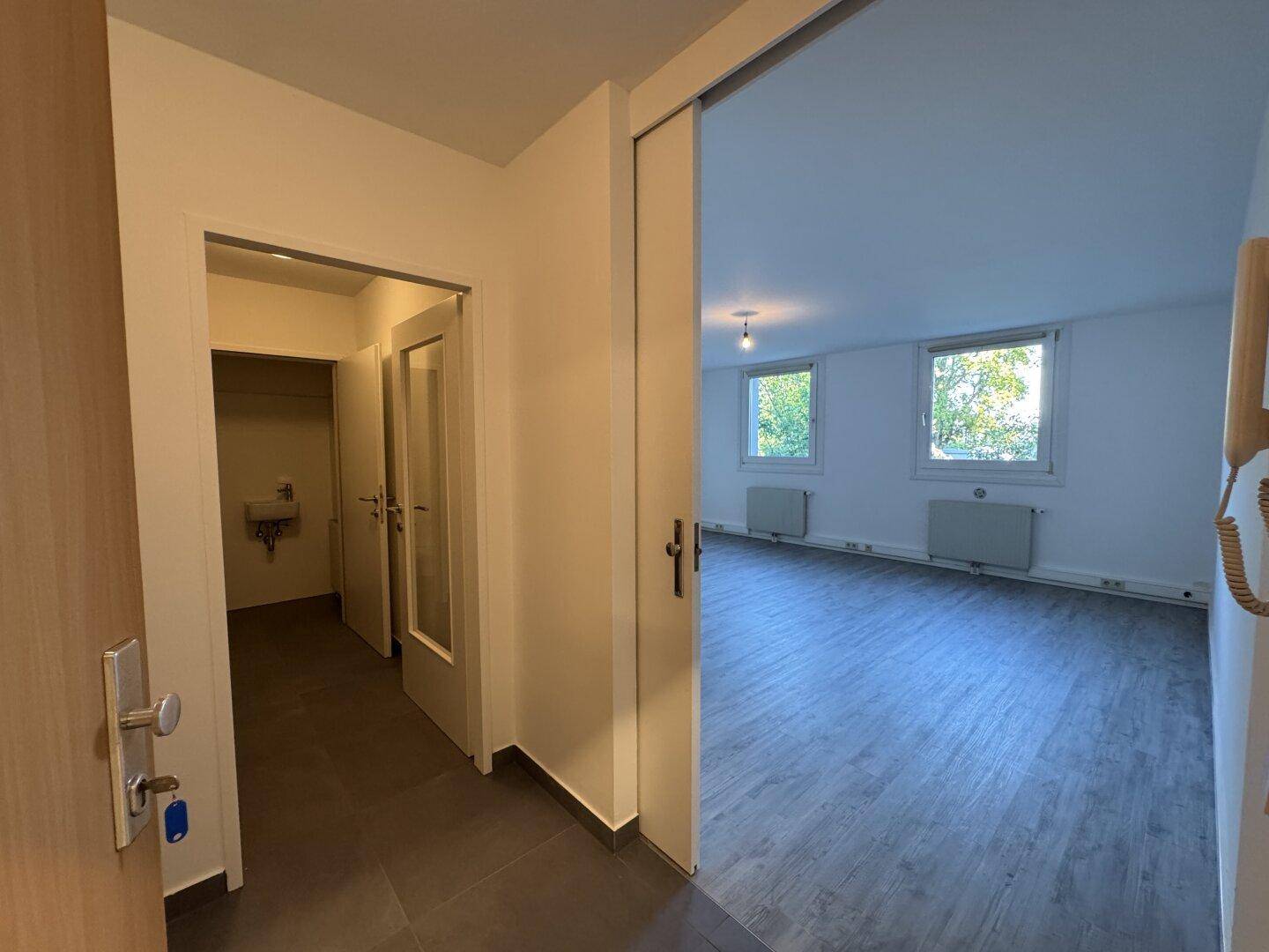 Eingangsbereich mit dunklen Fliesen und Blick in einen hellen Raum mit Laminatboden.
