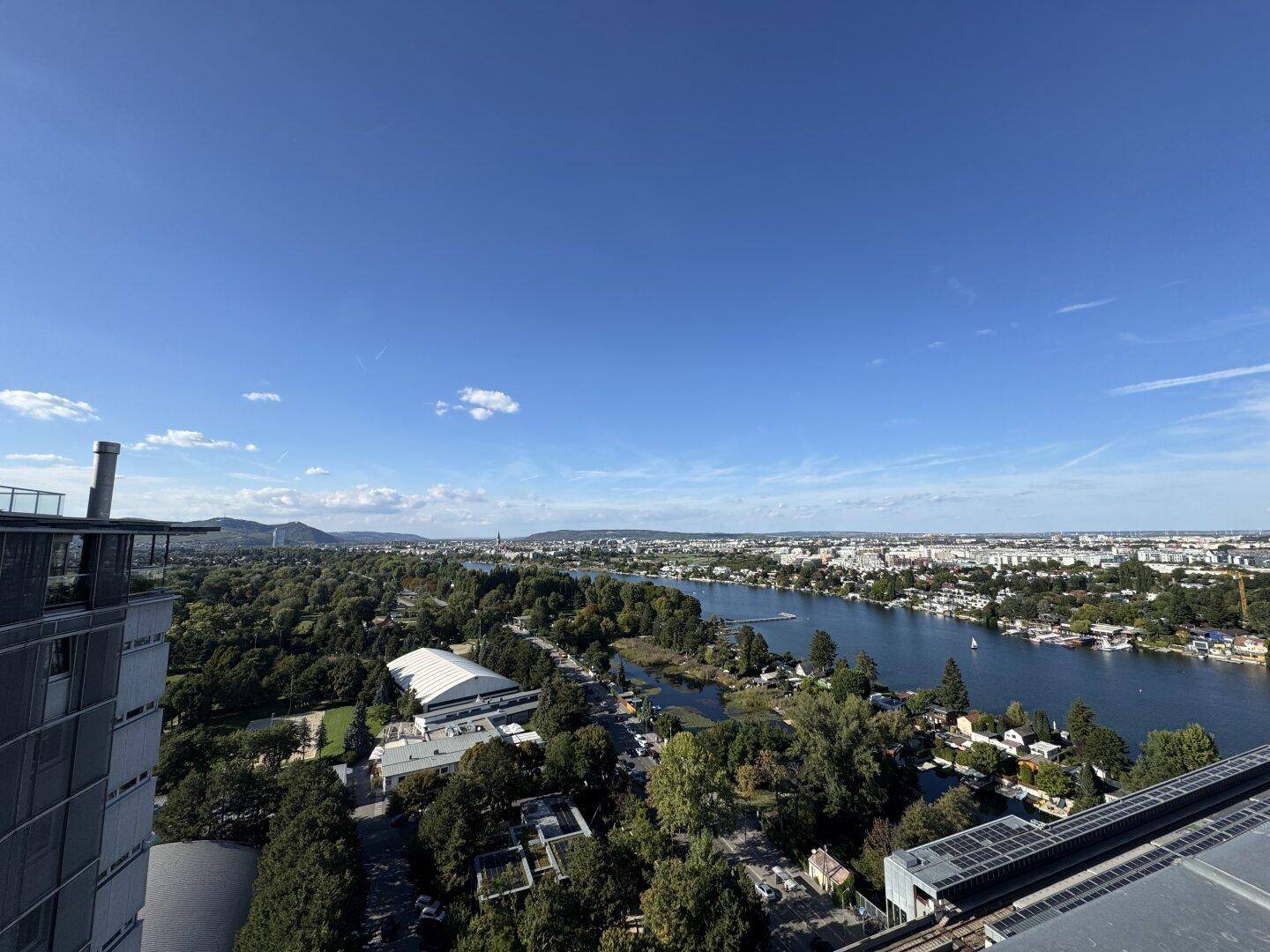 Weitläufiger Blick über die Stadt, den Fluss und grüne Landschaften unter strahlend blauem Himmel.