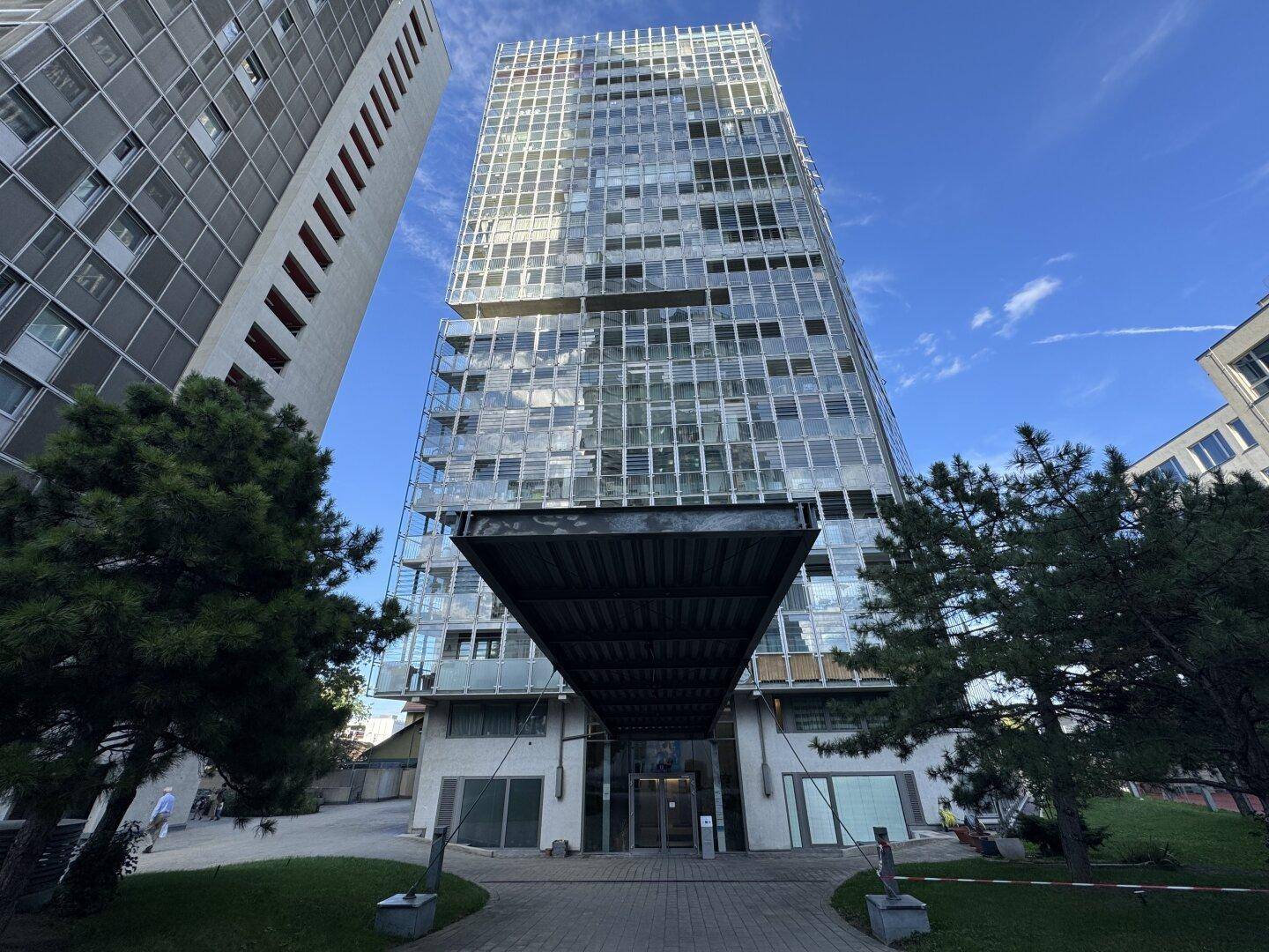 Moderne Hochhausfassade mit vielen Glasflächen und Balkonen unter blauem Himmel.