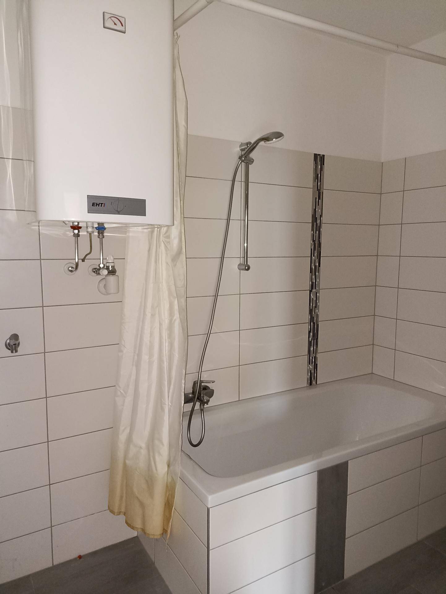 Badezimmer mit Badewanne, Duschvorhang und einem an der Wand montierten Warmwasserbereiter.