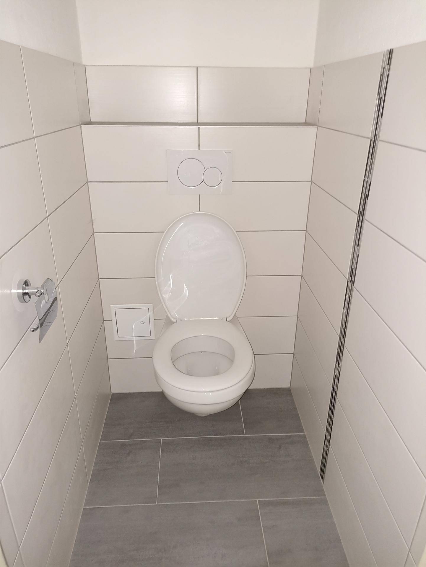 Separates WC mit wandhängender Toilette und weißen Fliesen an Wänden und Boden.