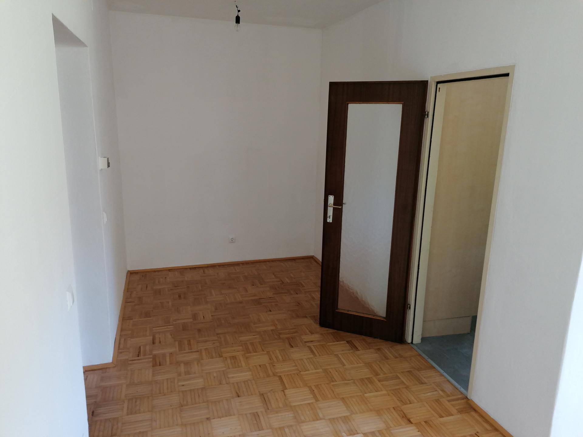 Leerer Raum mit hellem Parkettboden und einer Holztür mit Glaseinsatz.