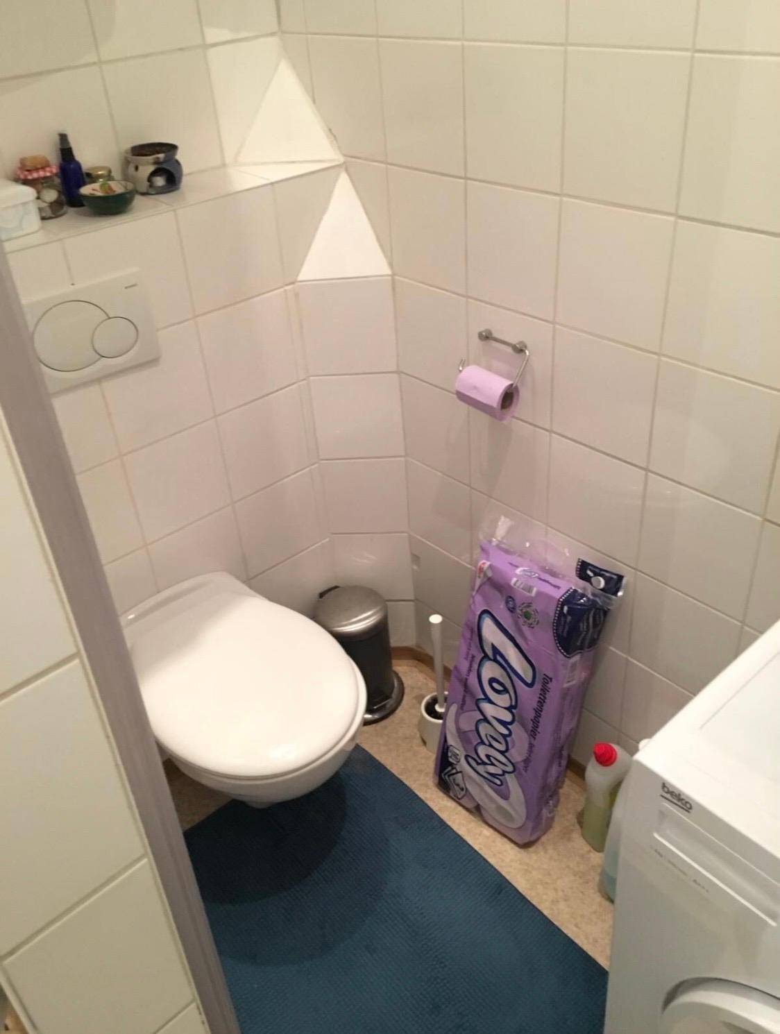 Separates WC mit wandhängender Toilette, weißen Fliesen und einer Waschmaschine.