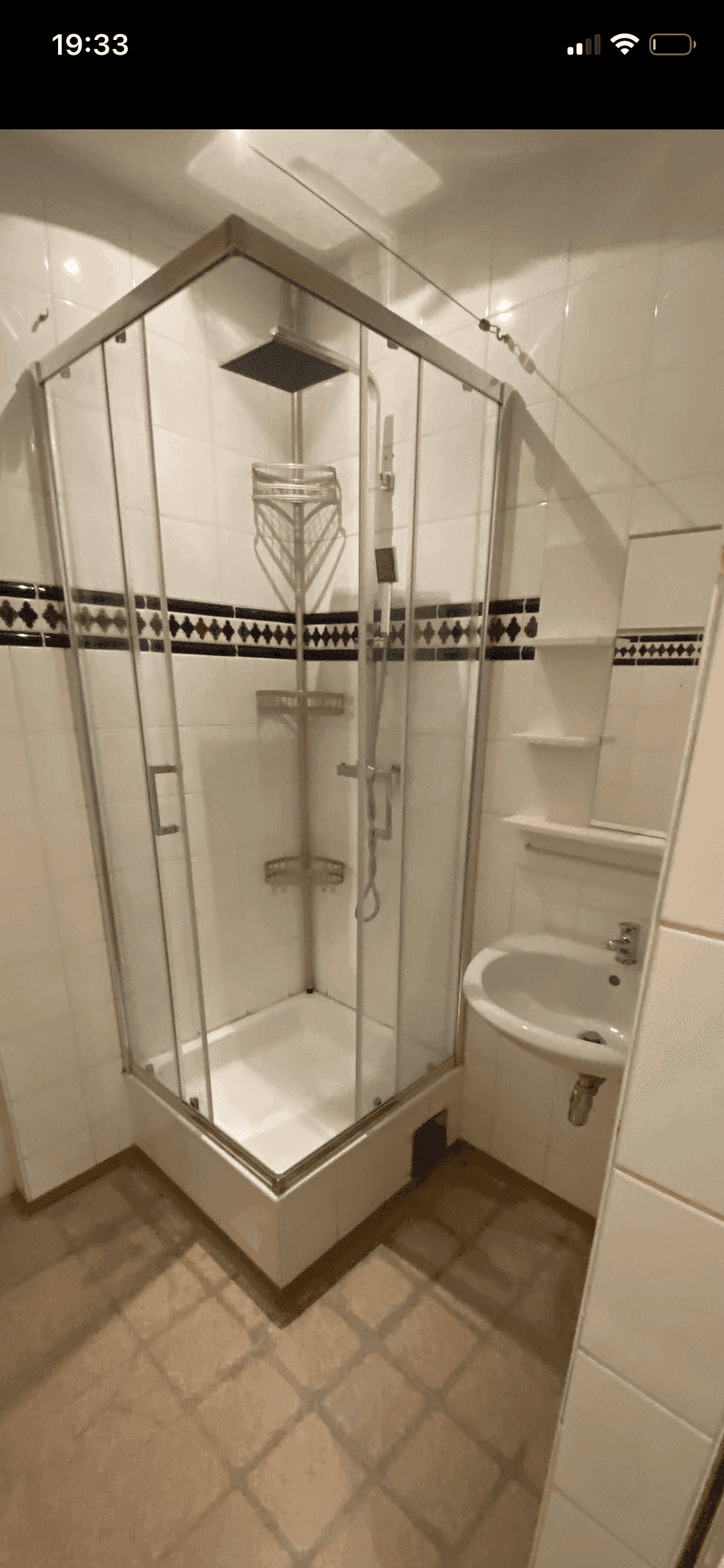 Badezimmer mit Duschkabine, kleinem Waschbecken und weißen Fliesen an Wänden und Boden.