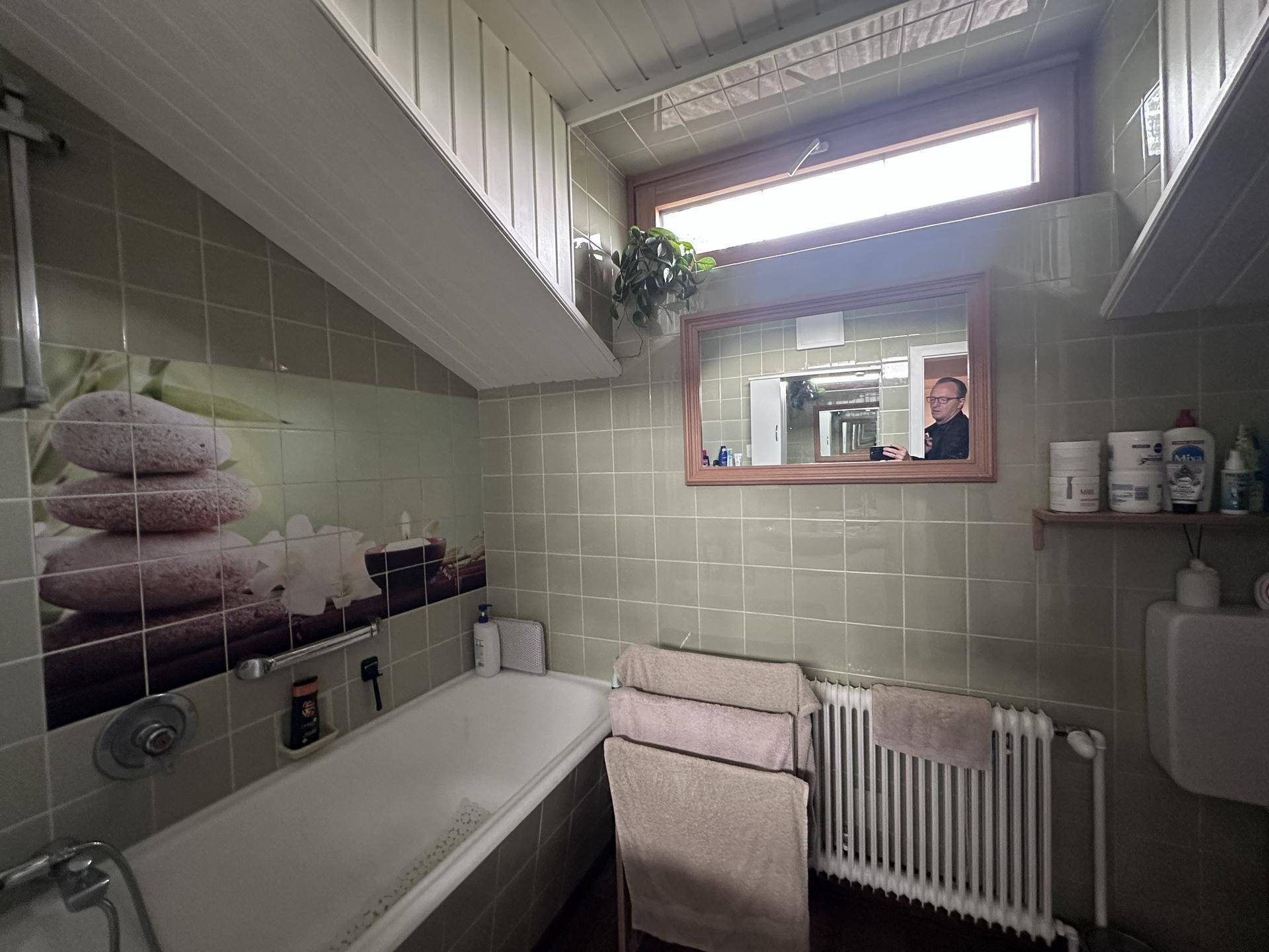 Badezimmer mit Badewanne, Fliesenboden und Fenster, in einem älteren Stil gehalten.