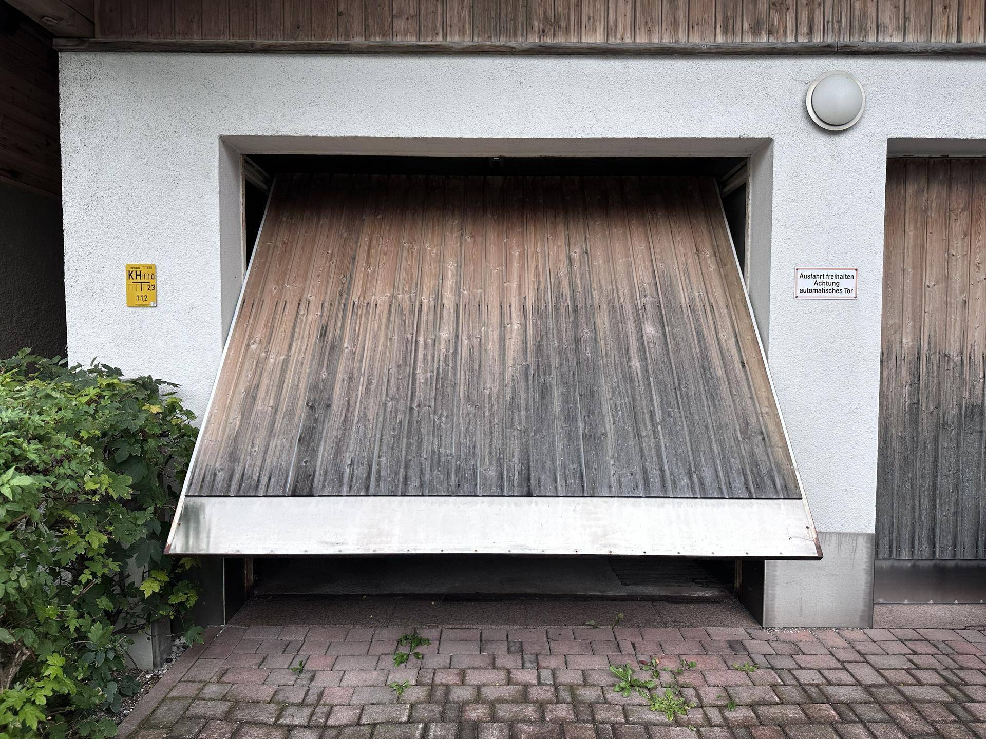 Garage mit einem teilweise geöffneten Holztor und gepflastertem Vorplatz.