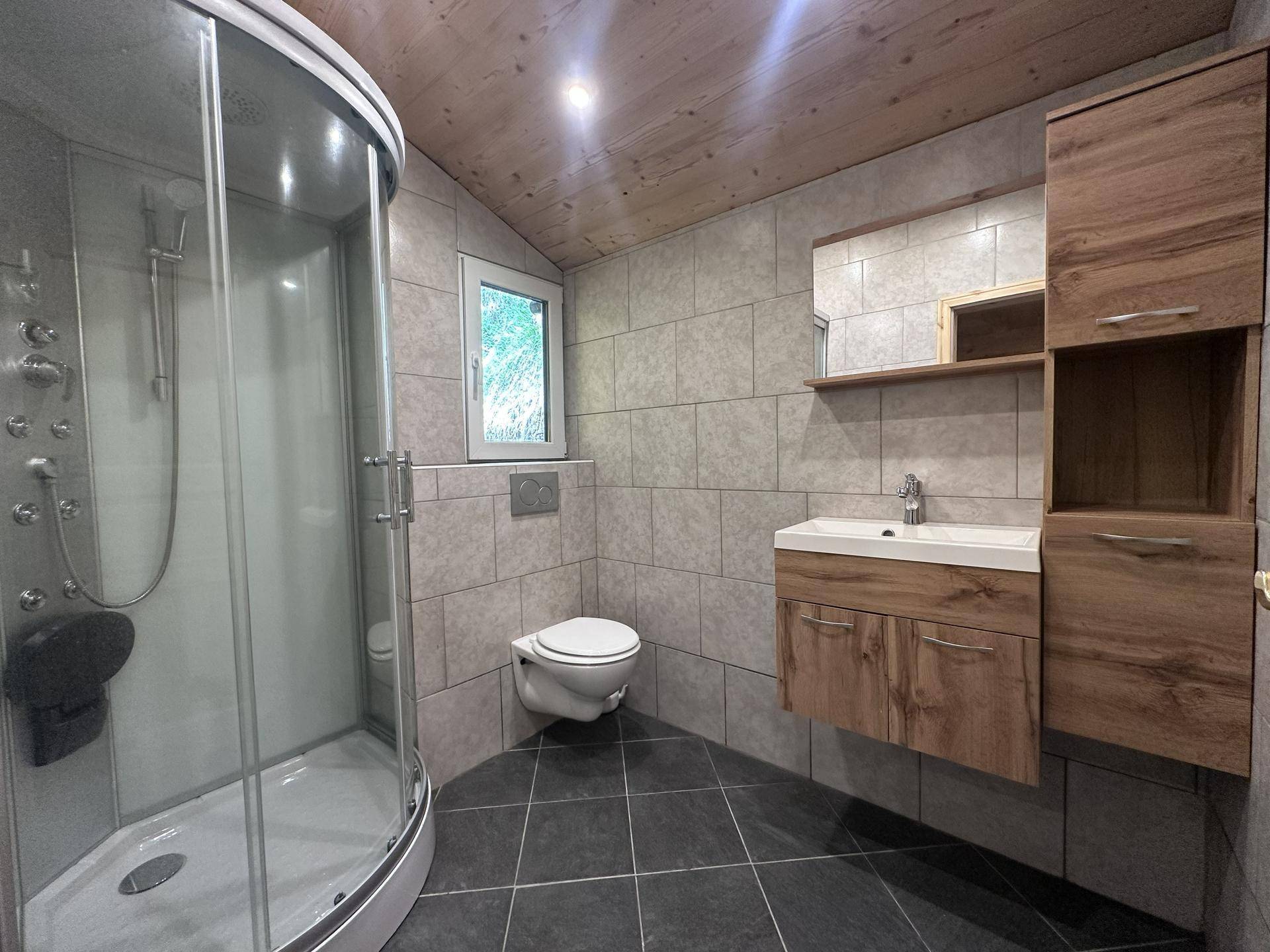 Modernes Badezimmer mit Duschkabine, Wand-WC, Holzwaschtisch und Fenster.