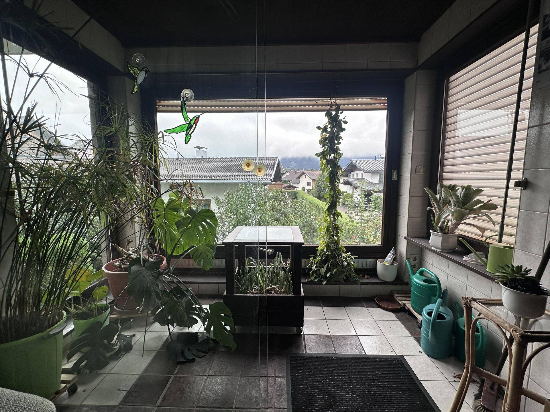 Wintergarten mit vielen Pflanzen, Fliesenboden und weitem Blick in die Umgebung.