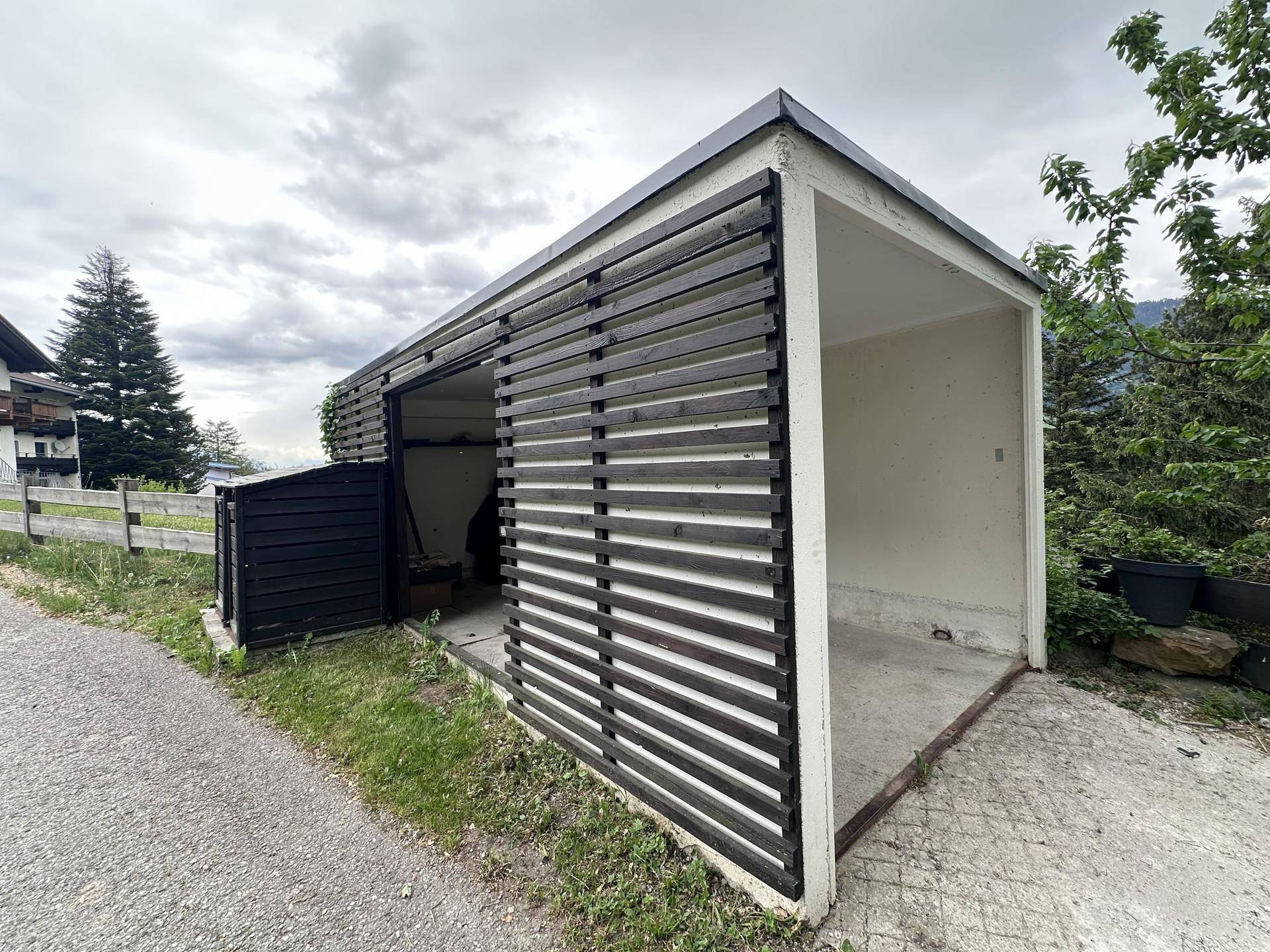 Offener Carport mit Holzlamellen und angrenzendem Abstellbereich.