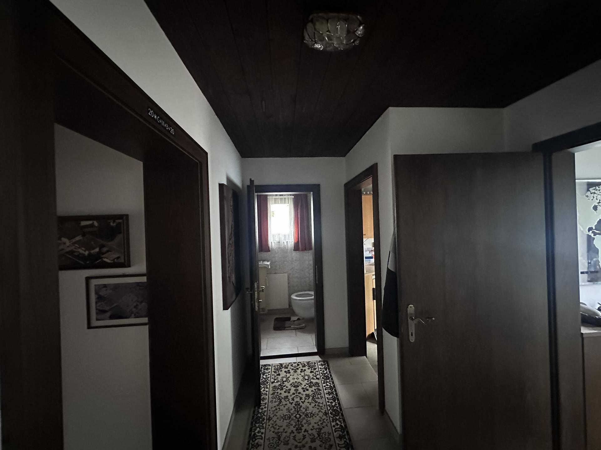 Dunkler Flur mit Holztürrahmen und Blick in ein Badezimmer mit Toilette.