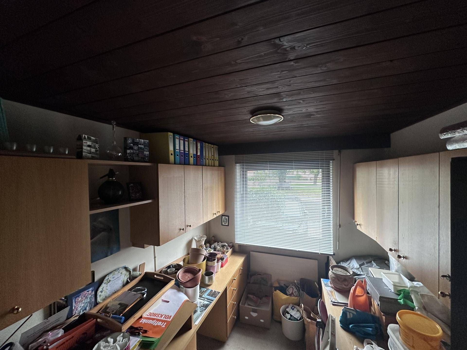 Abstellraum mit Holzdecke, Regalen und einem Fenster mit Blick ins Grüne.