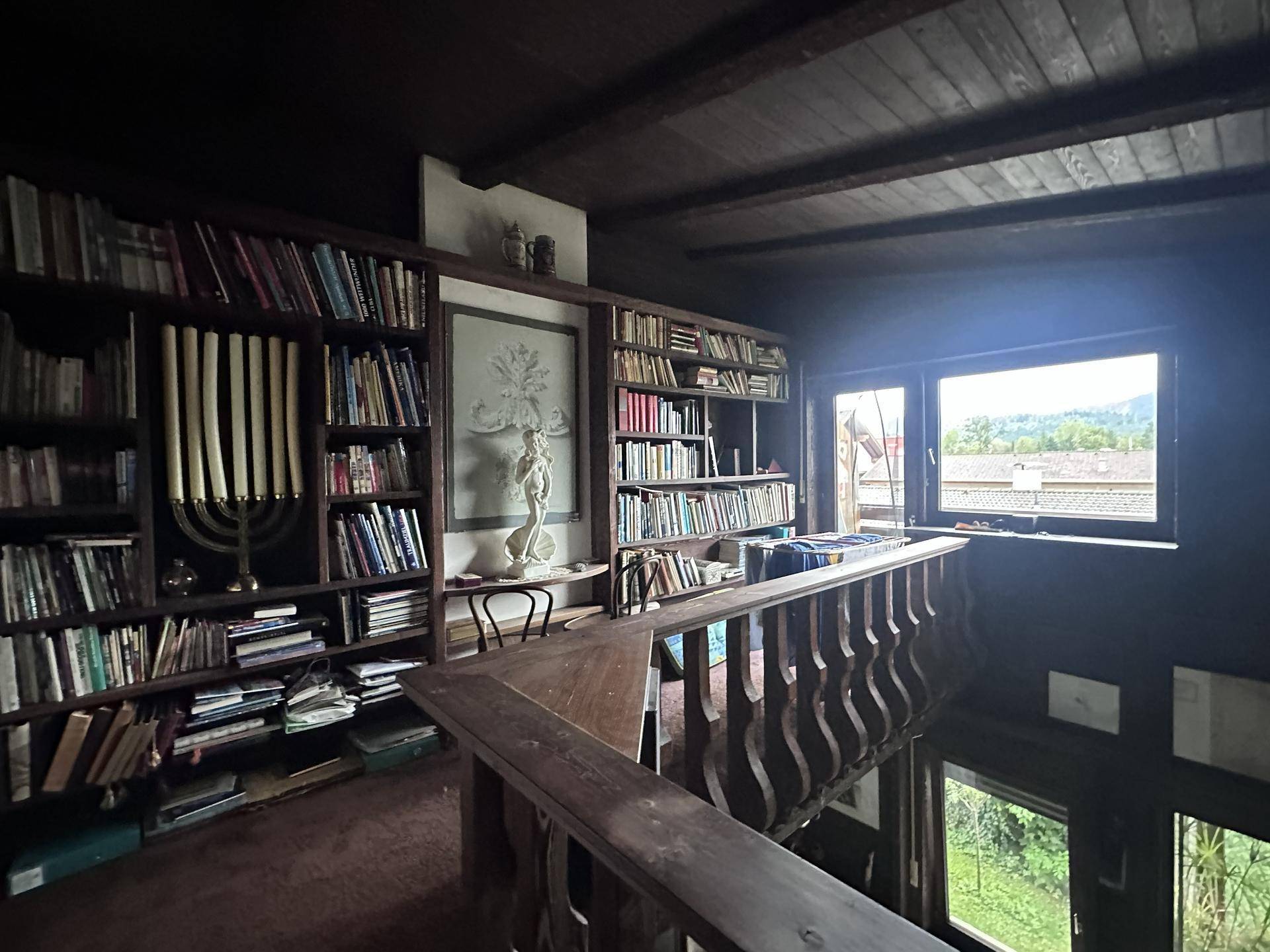 Dunkler Bibliotheksbereich mit vielen Büchern, Holzbalkendecke und Blick auf die Umgebung.