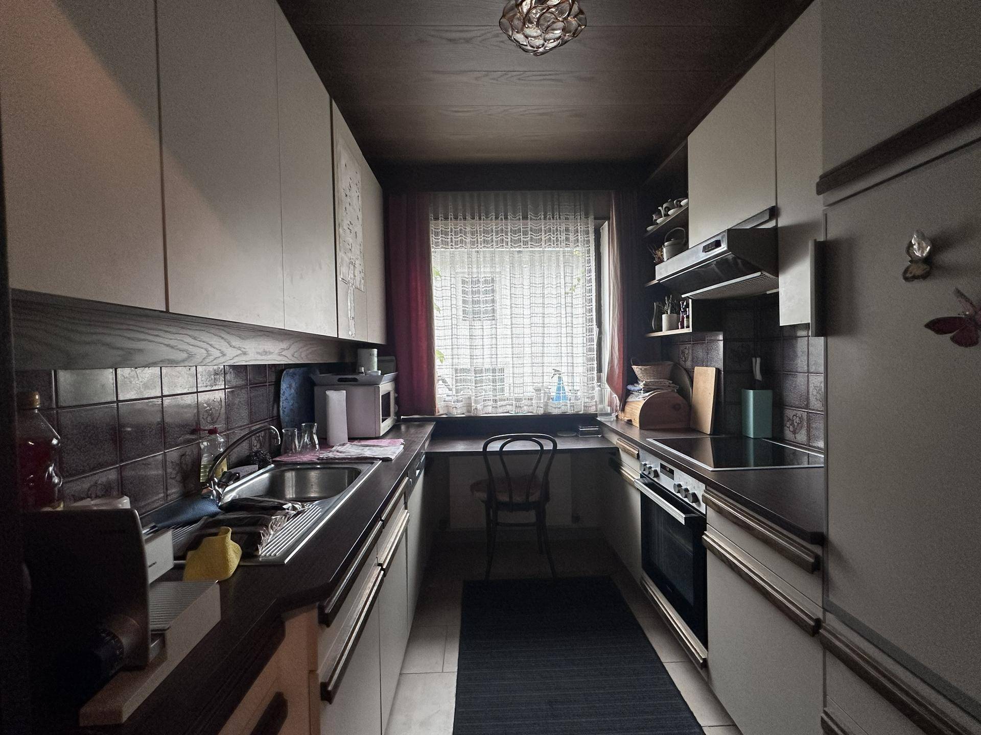 Schmale Küche mit dunklen Arbeitsplatten, gemusterten Fliesen und Fenster.
