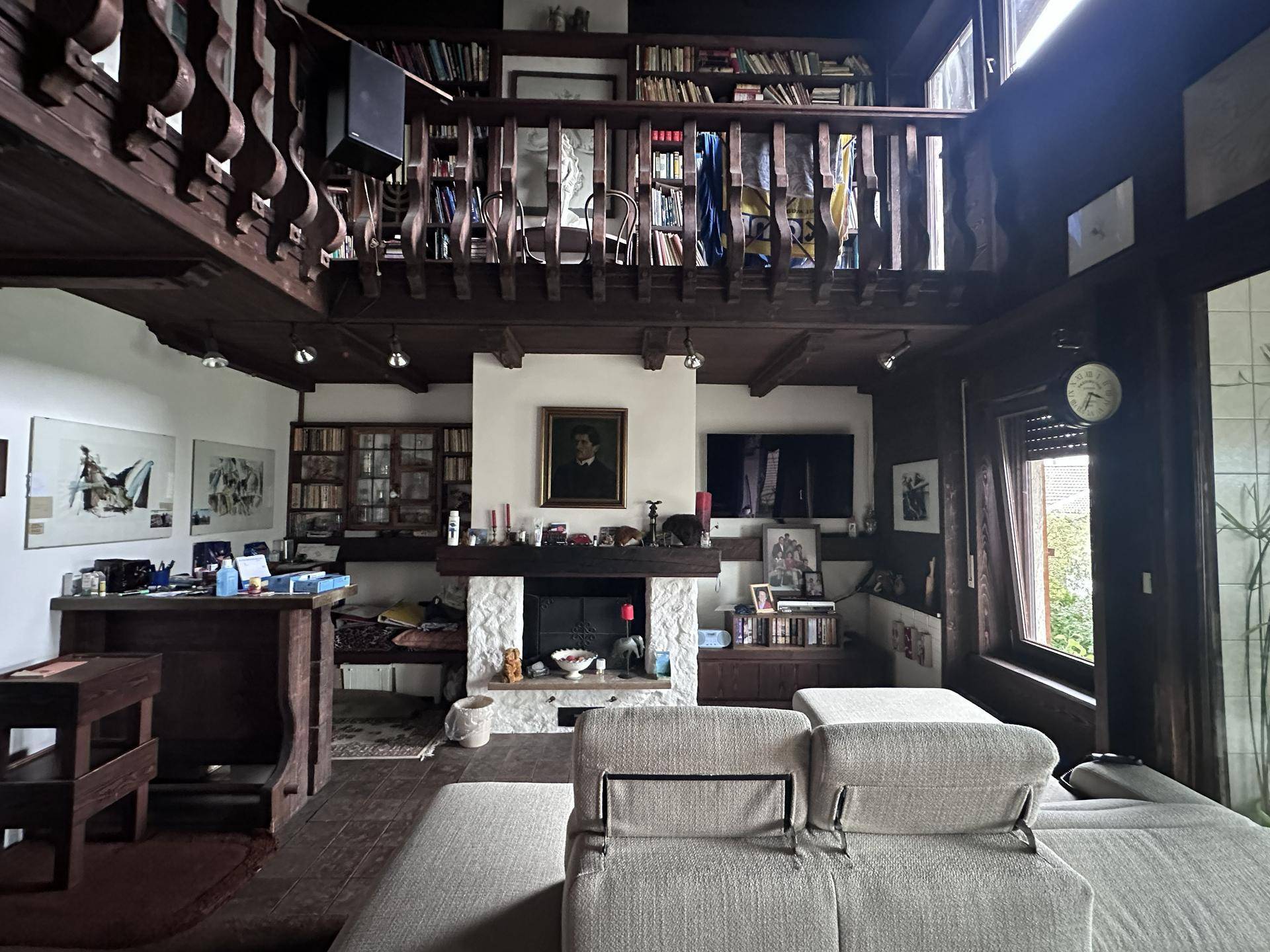 Rustikales Wohnzimmer mit Holzbalkendecke, Kamin und Galeriebereich mit Bücherregalen.