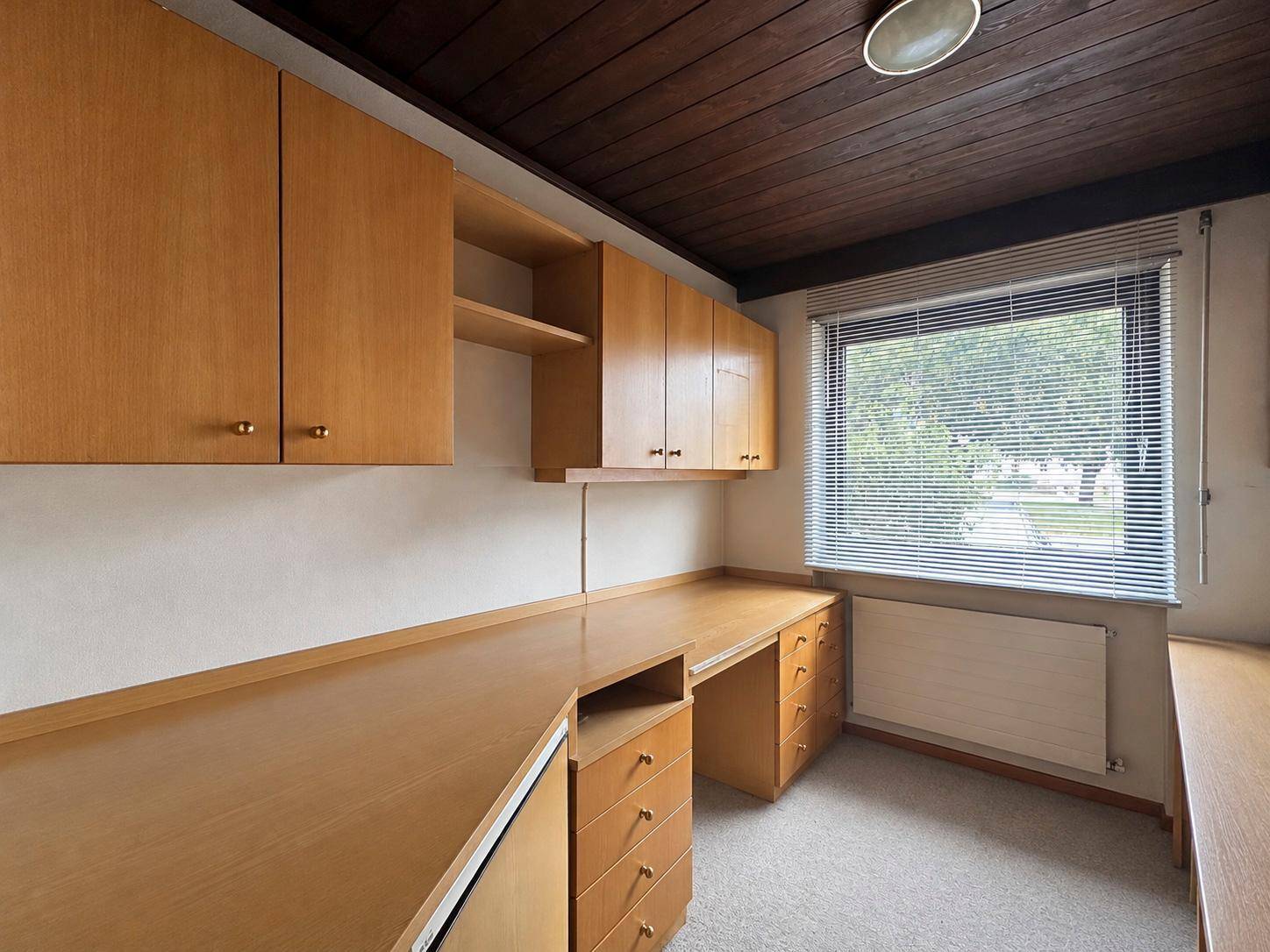 Helles Arbeitszimmer mit Holzschränken, großem Schreibtisch und Teppichboden.