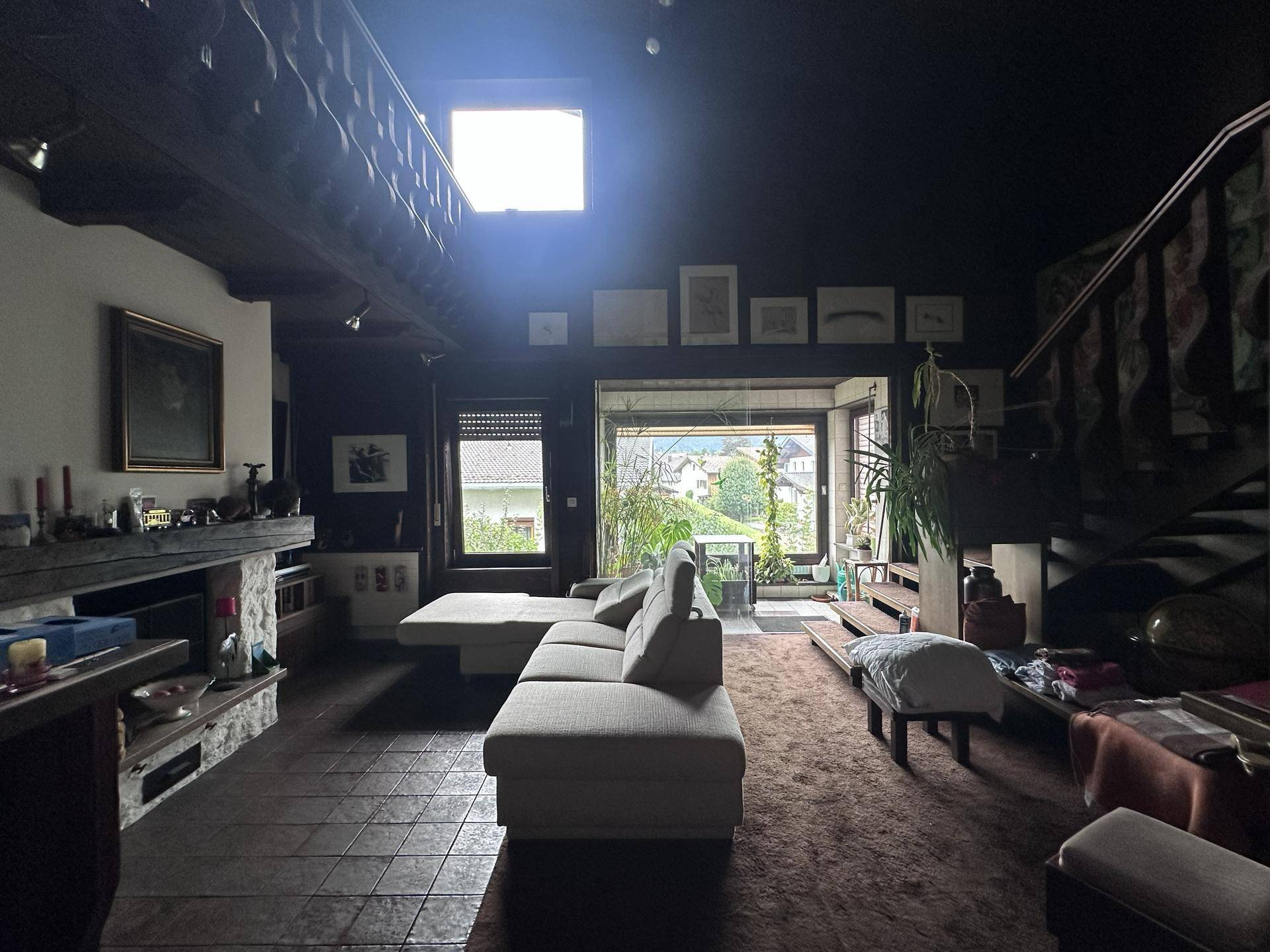 Geräumiges Wohnzimmer mit Holzbalkendecke, Kamin und Blick ins Grüne.