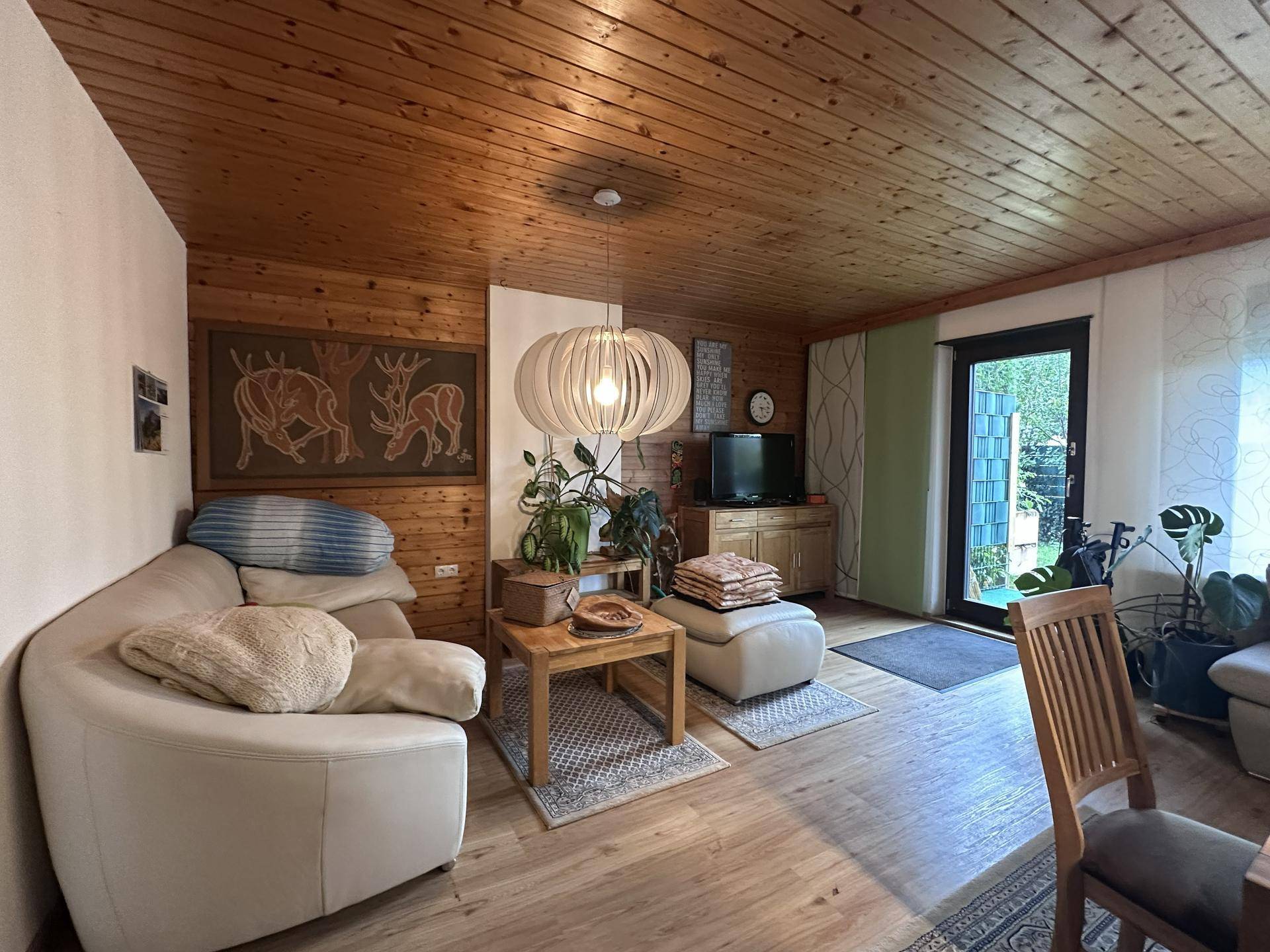 Wohnzimmer mit Holzdecke, bequemer Couch und Blick in den Garten.